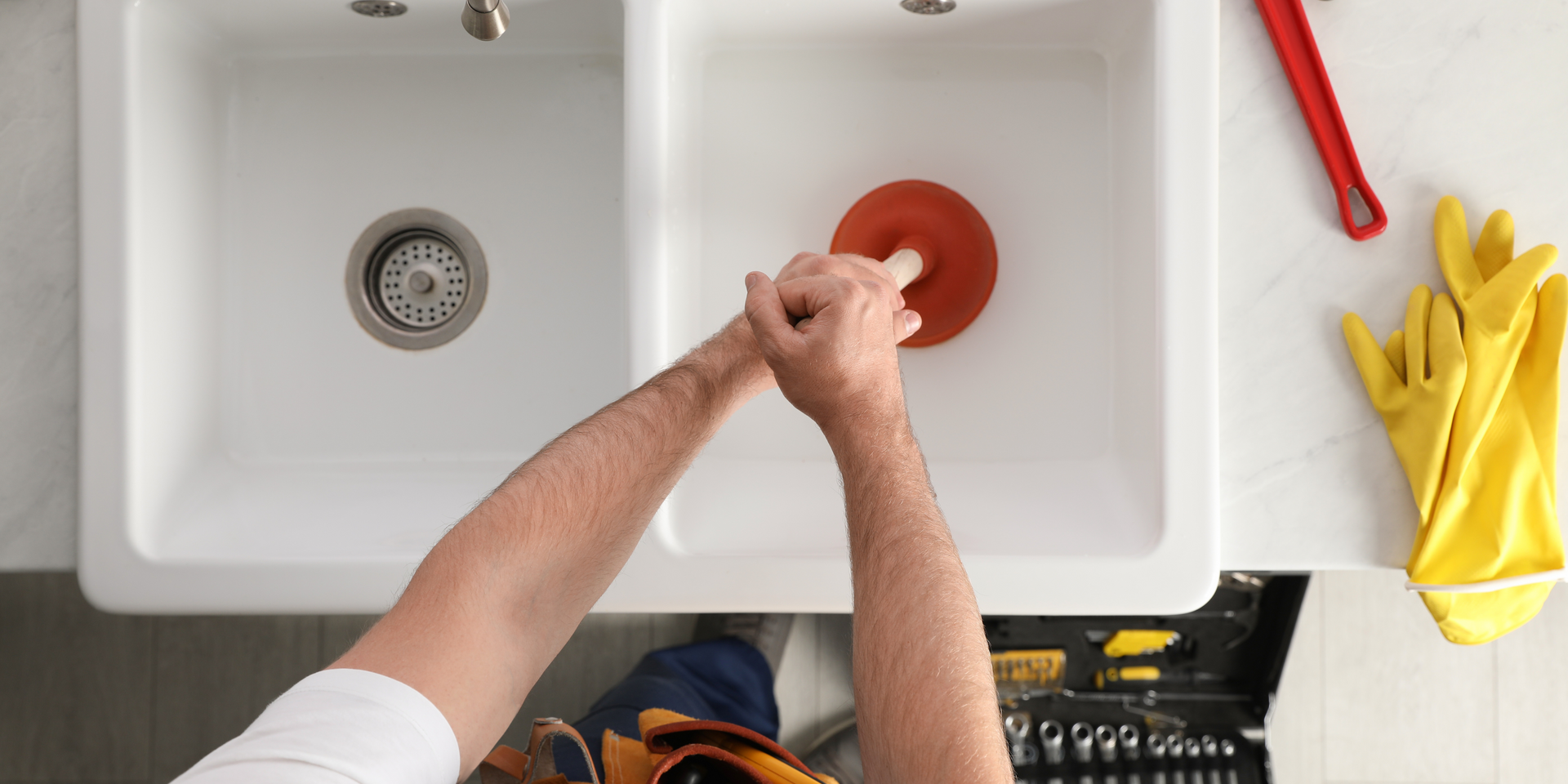 A man is using a plunger to unblock a kitchen sink.
