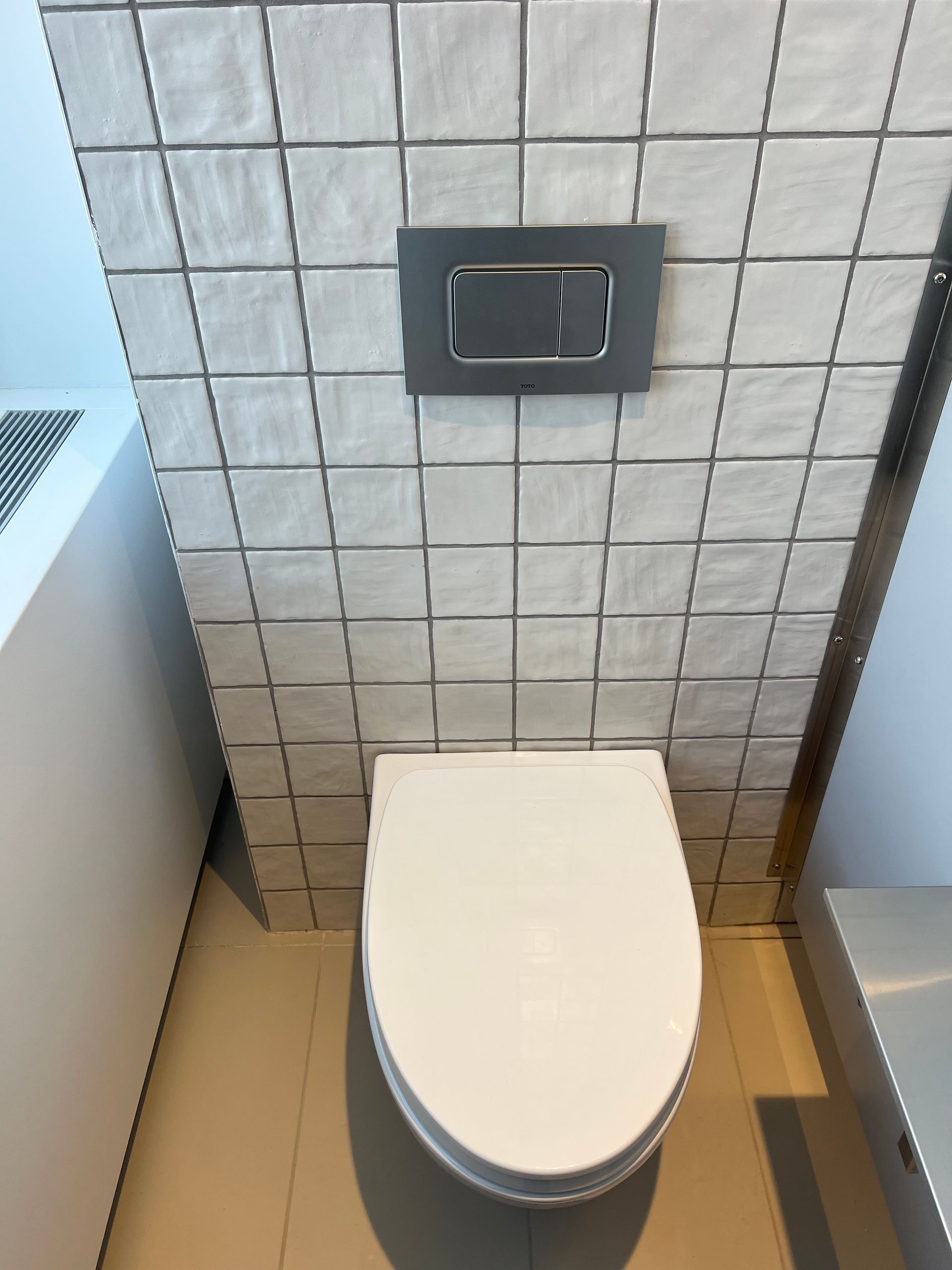A toilet in a bathroom with a tiled wall