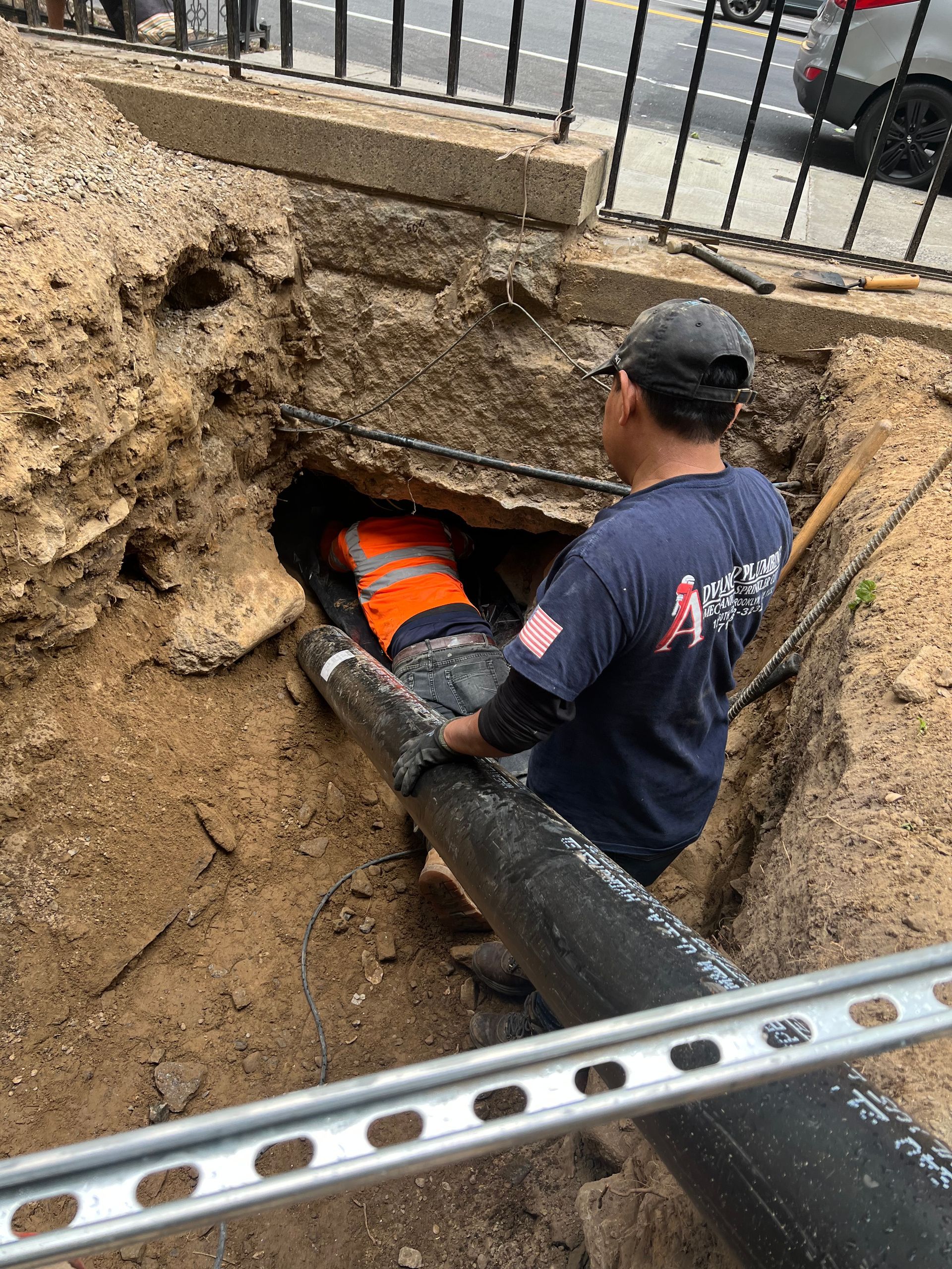 A man is sitting in a hole in the ground next to a pipe.