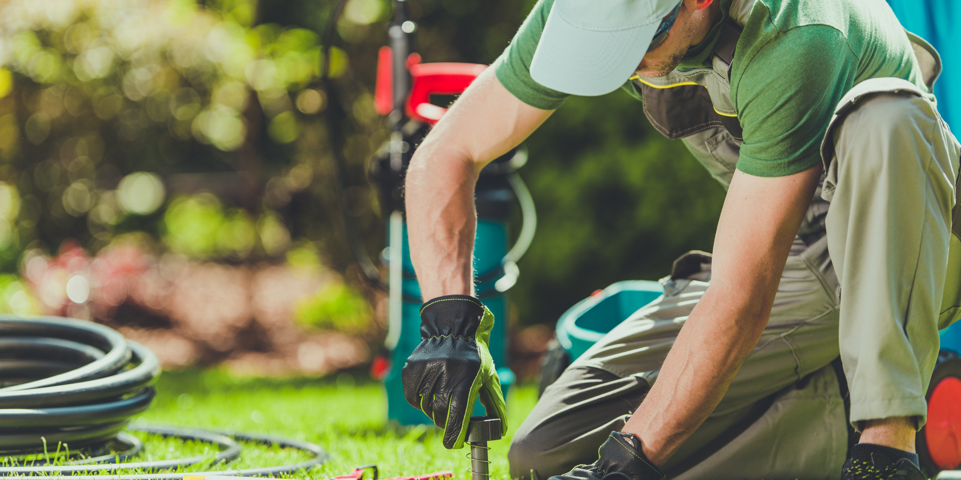 A man is kneeling down in the grass working on a lawn.