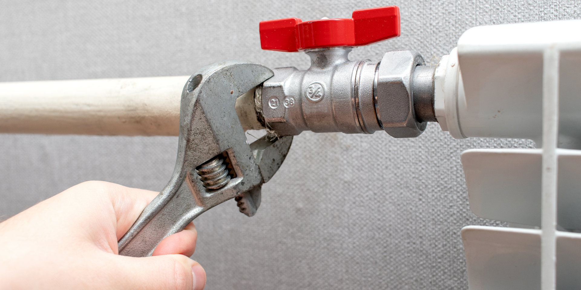 A person is fixing a radiator with a wrench.