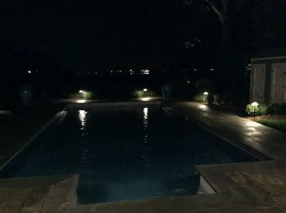 A rectangular backyard swimming pool at night, illuminated by soft landscape lights along the edge.