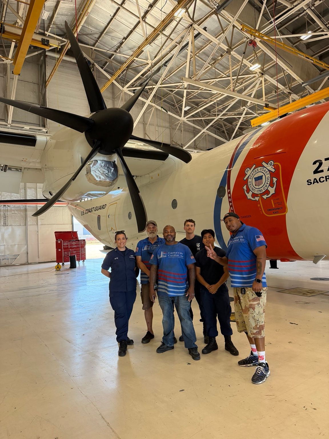 Capital City Comfort team and Coast Guard personnel beside an aircraft inside the Sacramento hangar
