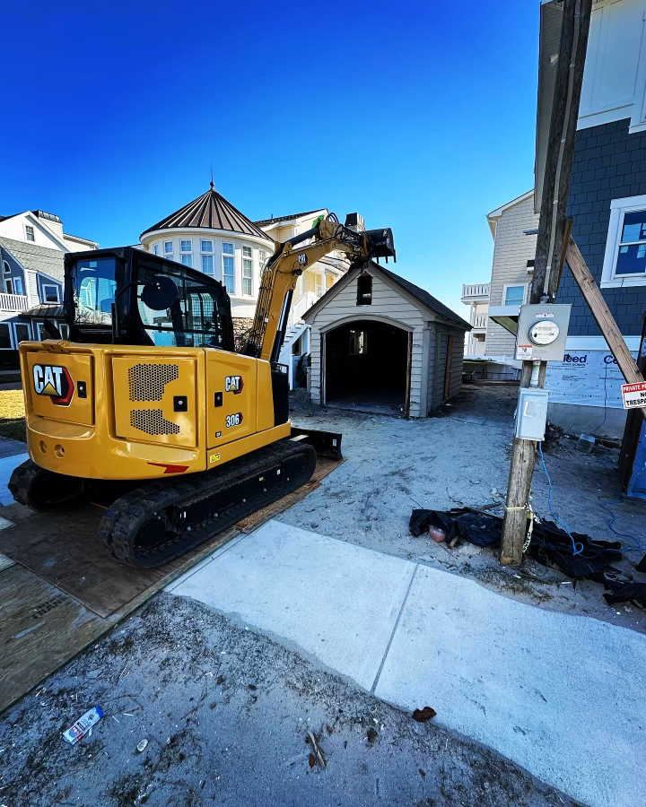A yellow cat excavator is parked in front of a garage