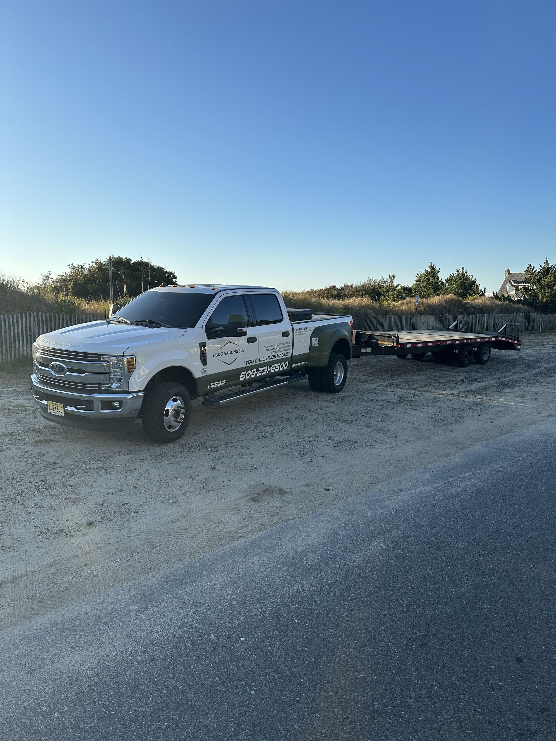 A white truck is parked in a gravel lot with a trailer attached to it