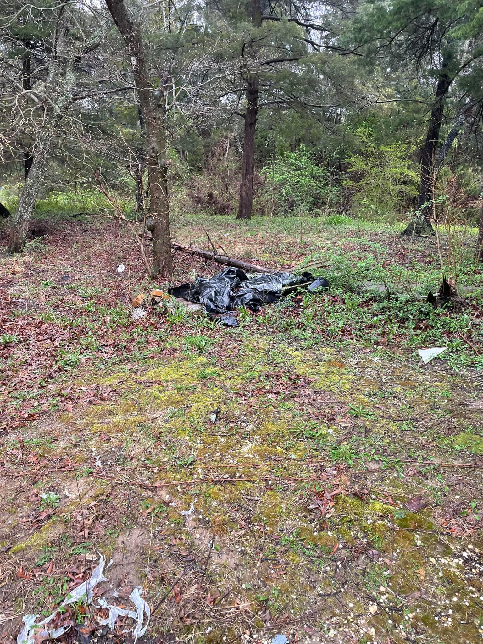 A pile of trash is laying on the ground in the middle of a forest