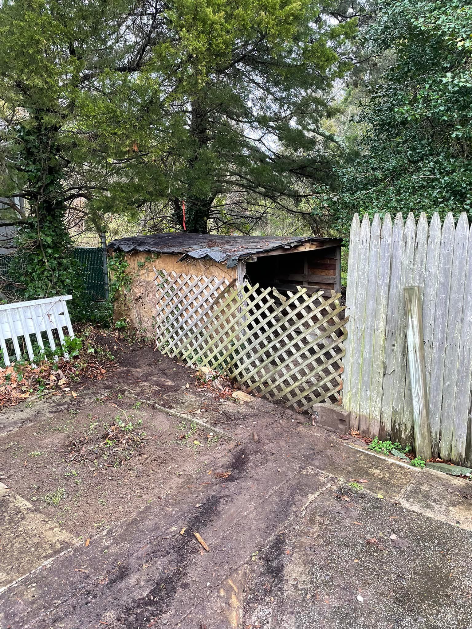 A dirt road leading to a shed behind a wooden fence
