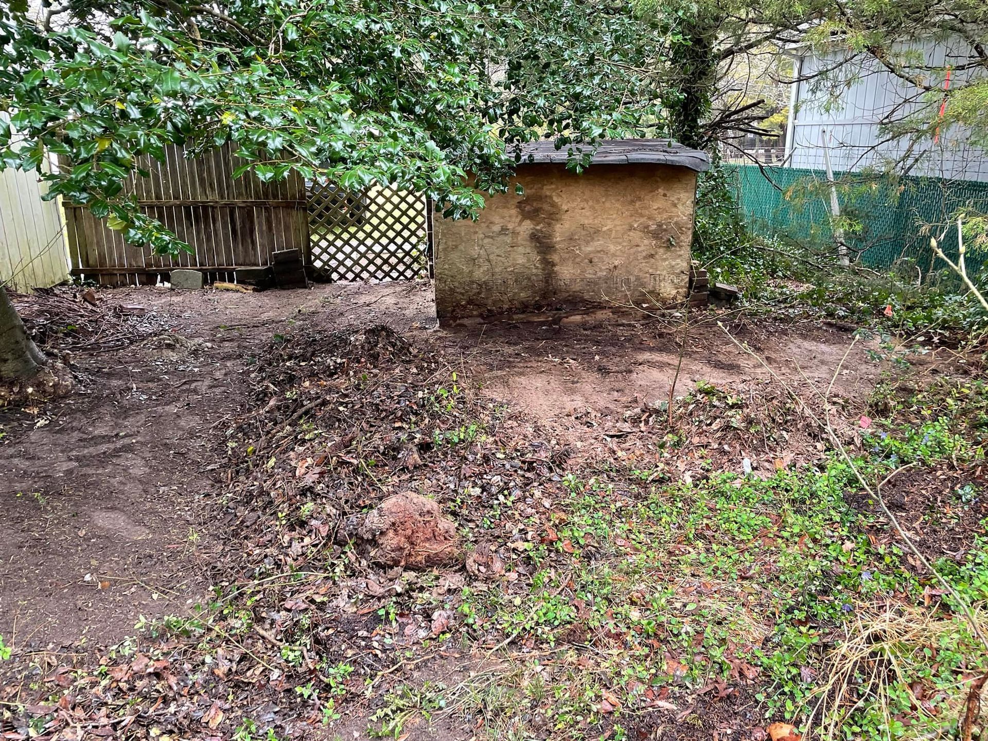 A dog house is sitting in the middle of a dirt field surrounded by trees