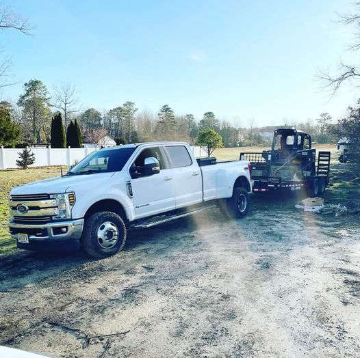 A white truck with a trailer attached to it is parked on a dirt road