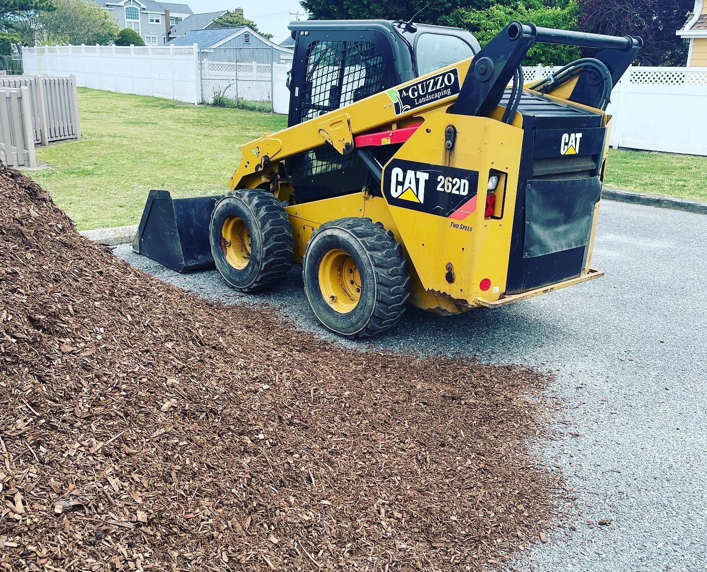 A yellow cat skid steer is loading a pile of mulch