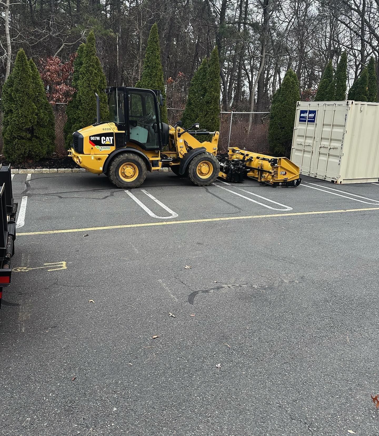 A yellow tractor is parked in a parking lot next to a white container