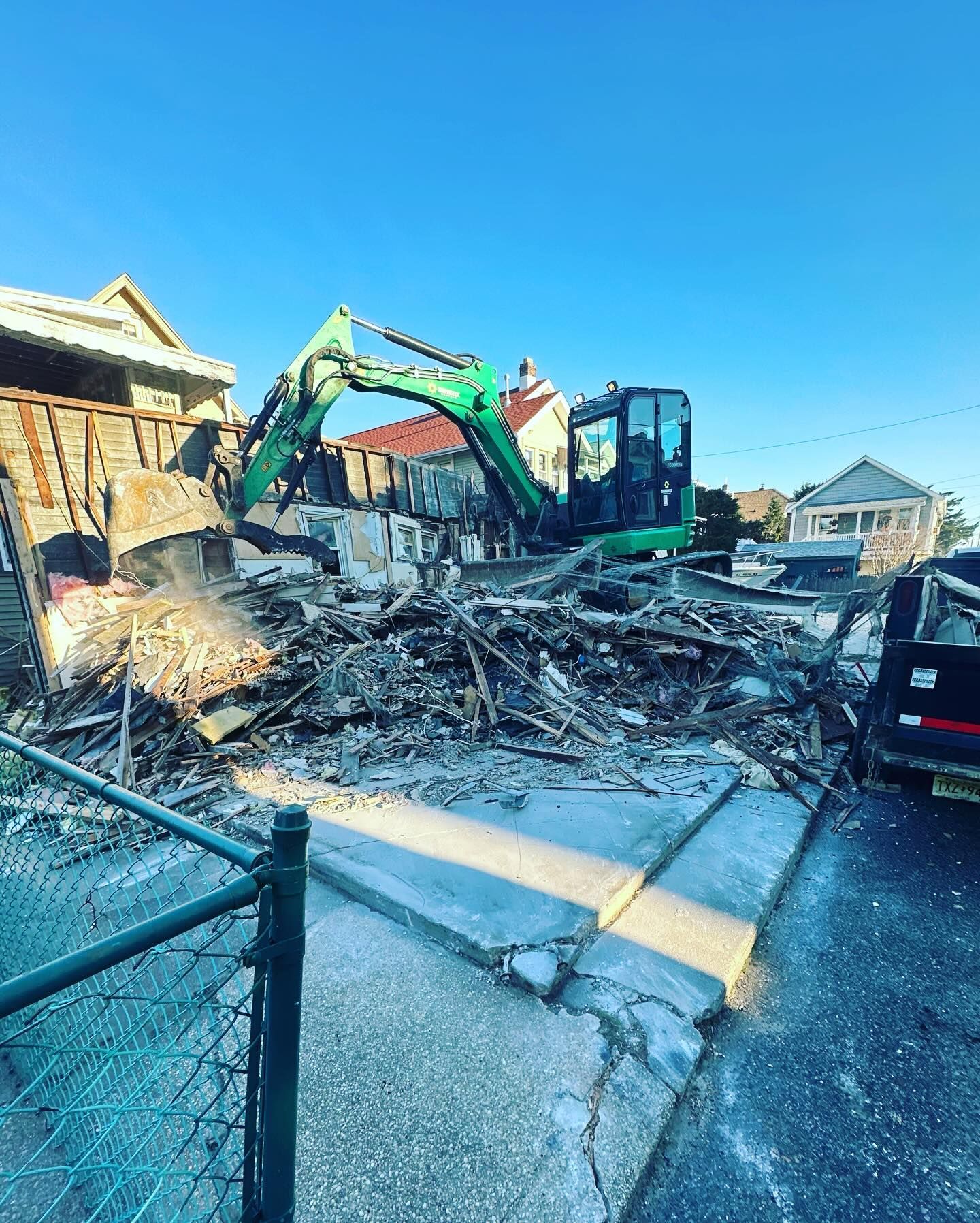A green excavator is demolishing a house on the side of the road