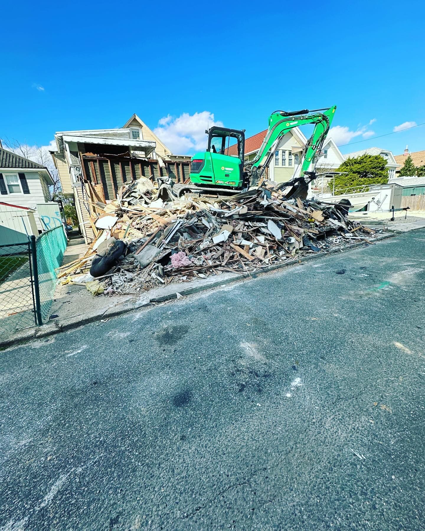 A green excavator is demolishing a house on the side of the road