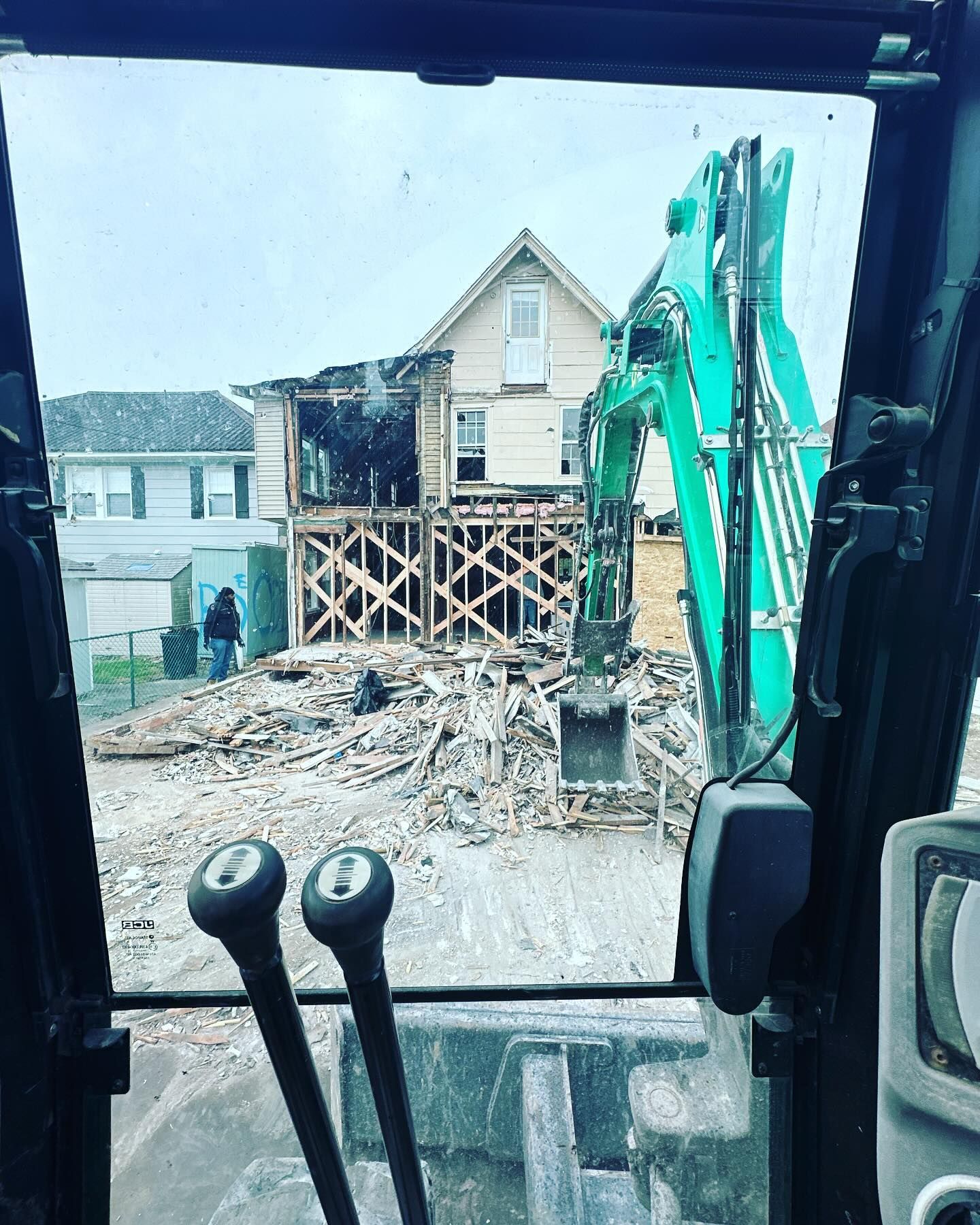 A house is being demolished by a green excavator