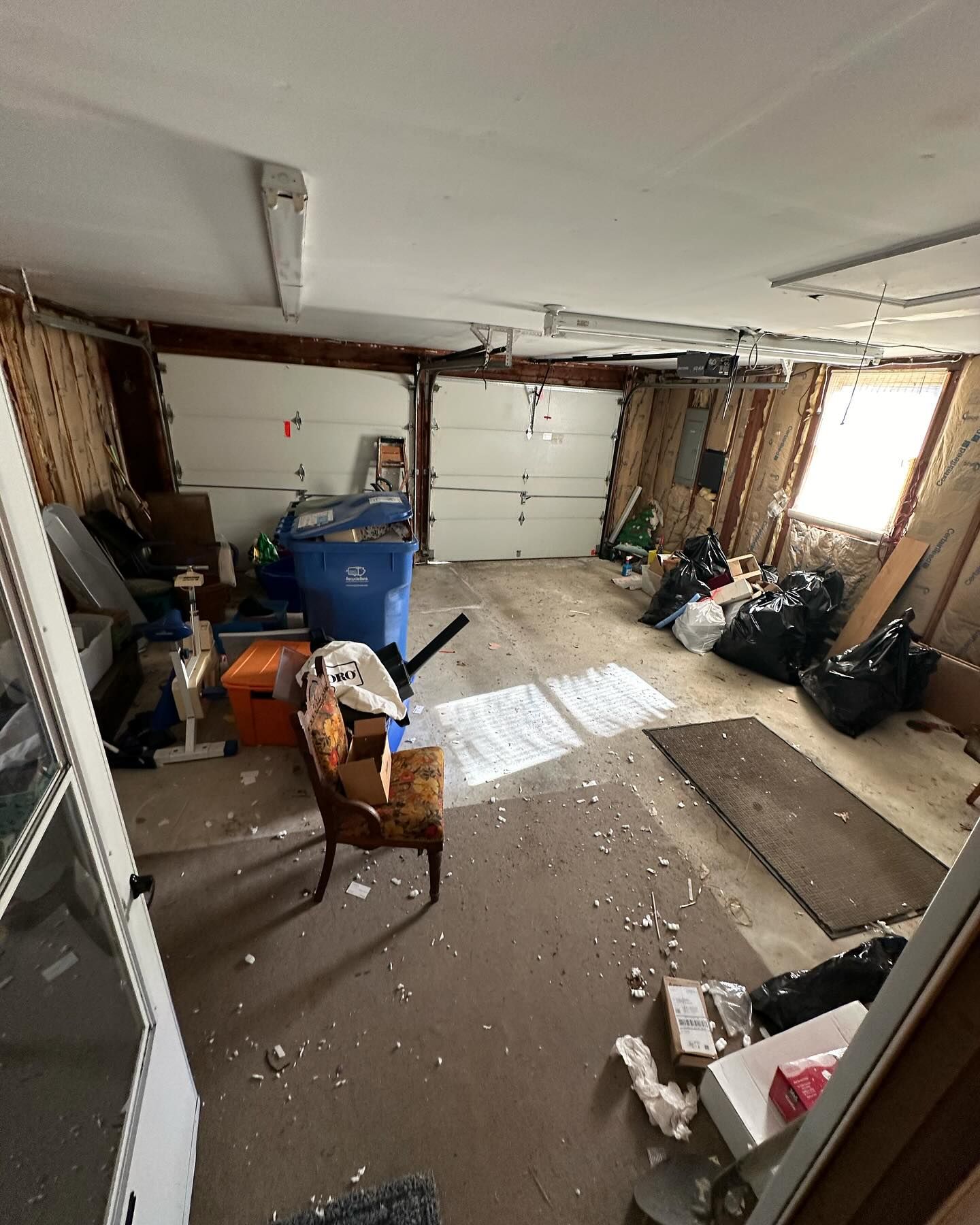 A messy garage with a chair and trash bags