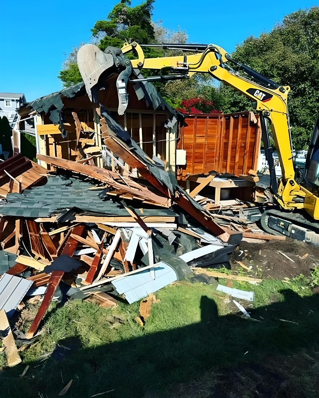 A large yellow excavator is demolishing a house