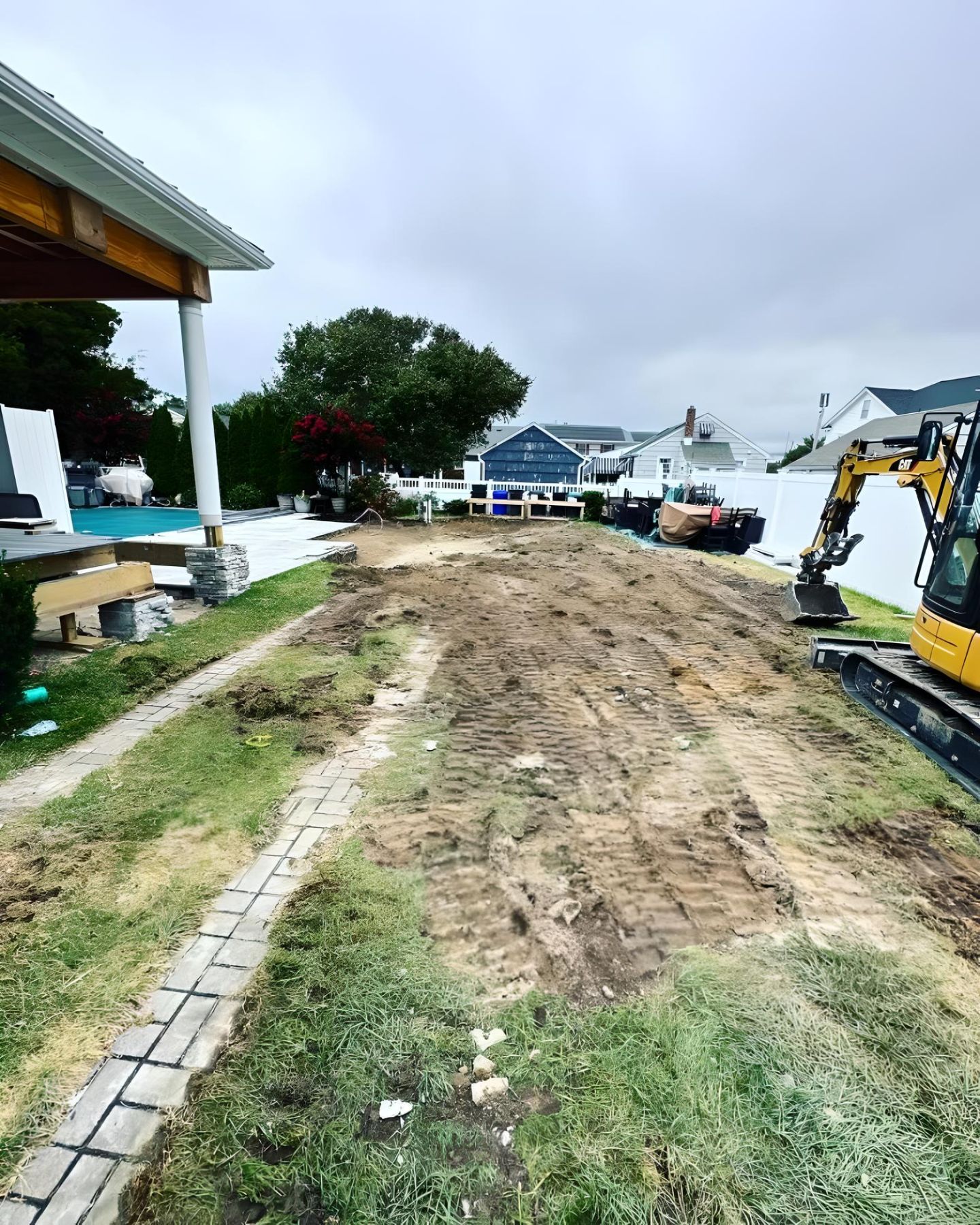 A yellow excavator is digging a dirt road in front of a house
