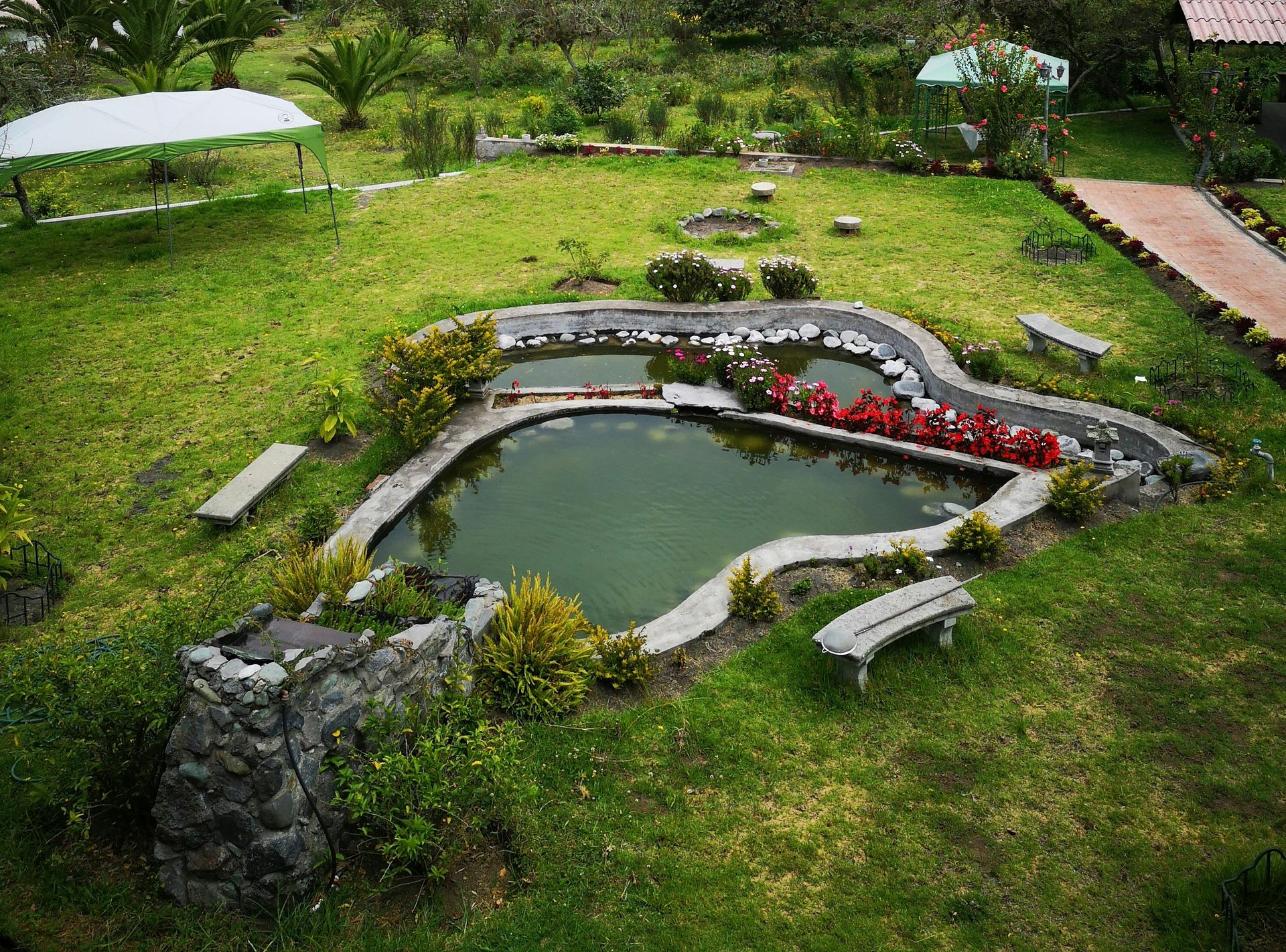 Pond with stone borders and benches, surrounded by green grass and flowers.