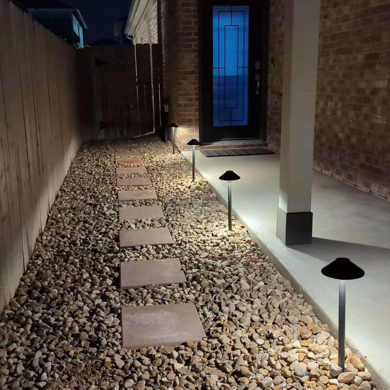 A walkway lined with bricks and gravel is lit up at night