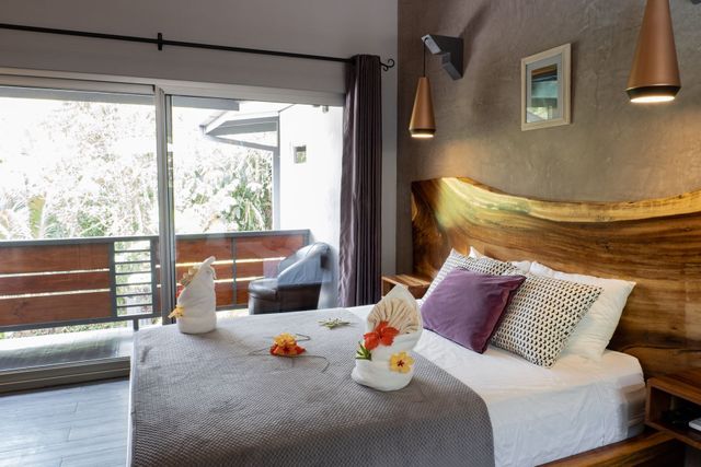 A hotel room with a wooden headboard, a bed with folded towel art, and sliding glass doors opening to a balcony.