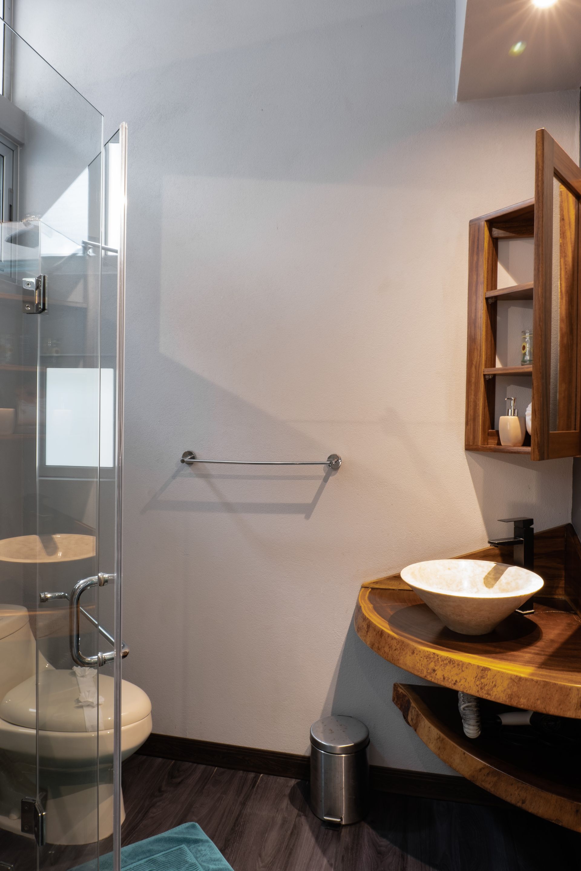 A modern bathroom featuring a live-edge wooden vanity with a white vessel sink, a glass-enclosed shower, and a toilet.