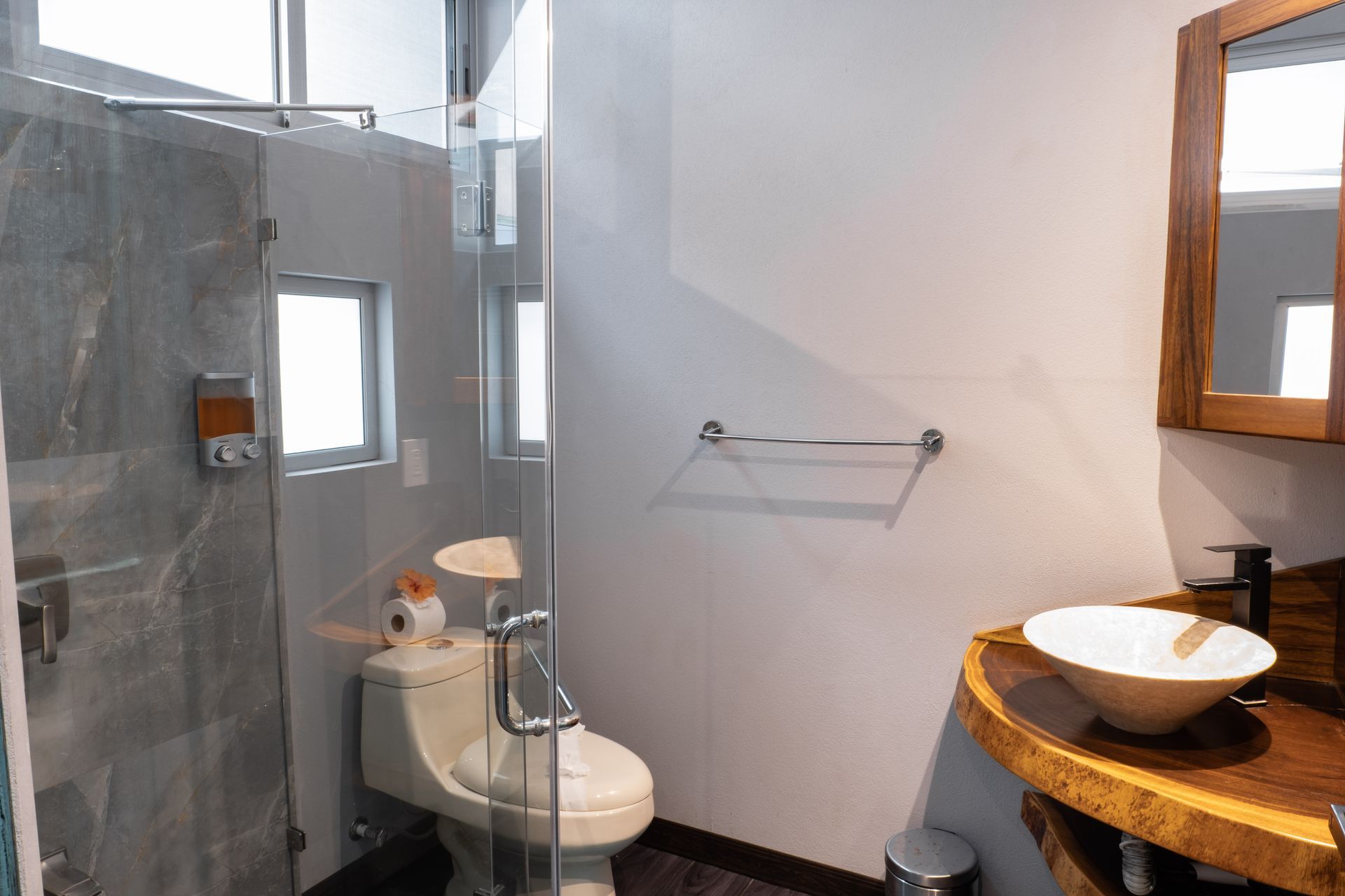 A modern bathroom featuring a live-edge wood vanity with a white vessel sink, a glass-enclosed shower, and a toilet.