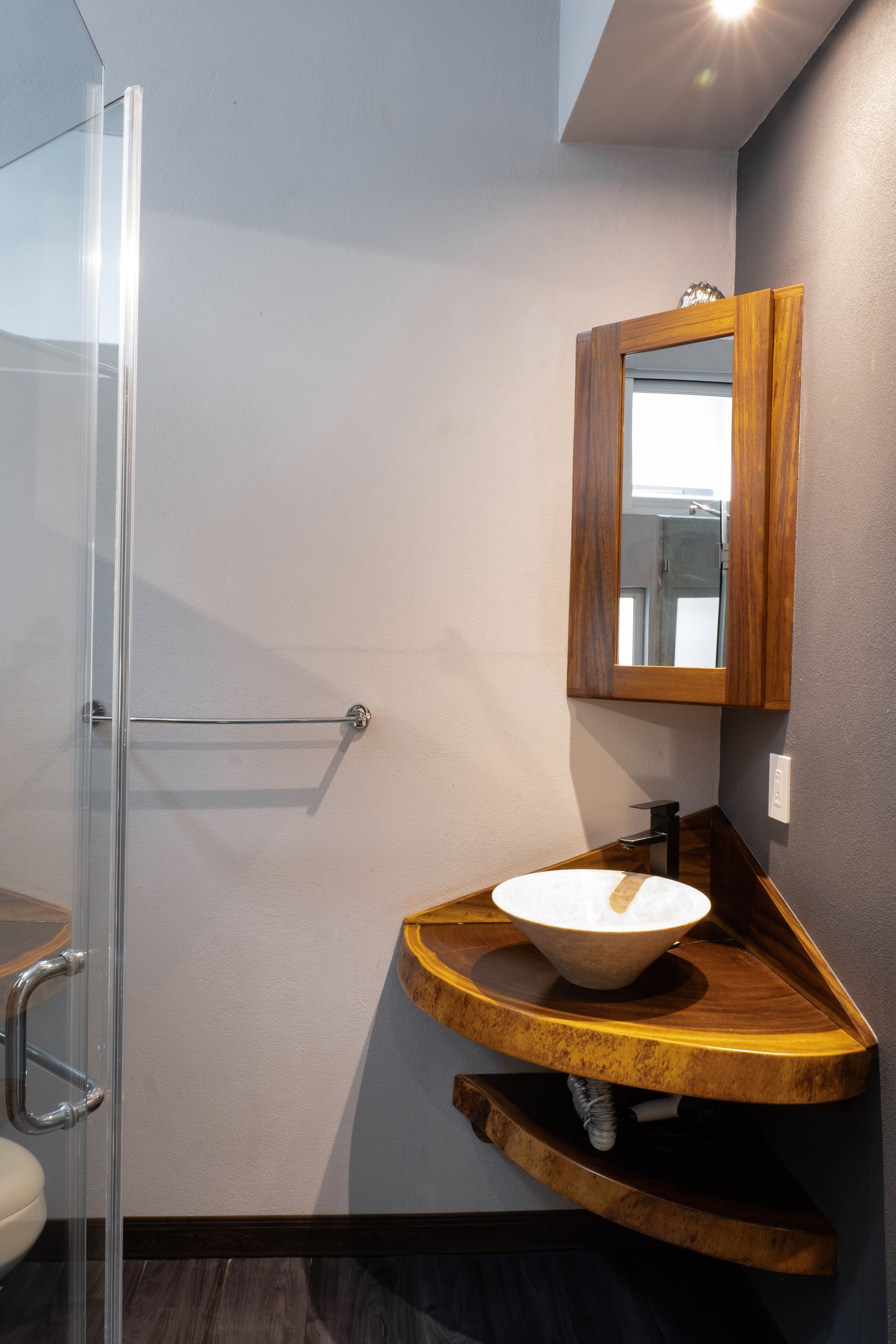 A corner bathroom vanity with a rustic wood counter, a white vessel sink, and a matching wooden medicine cabinet.