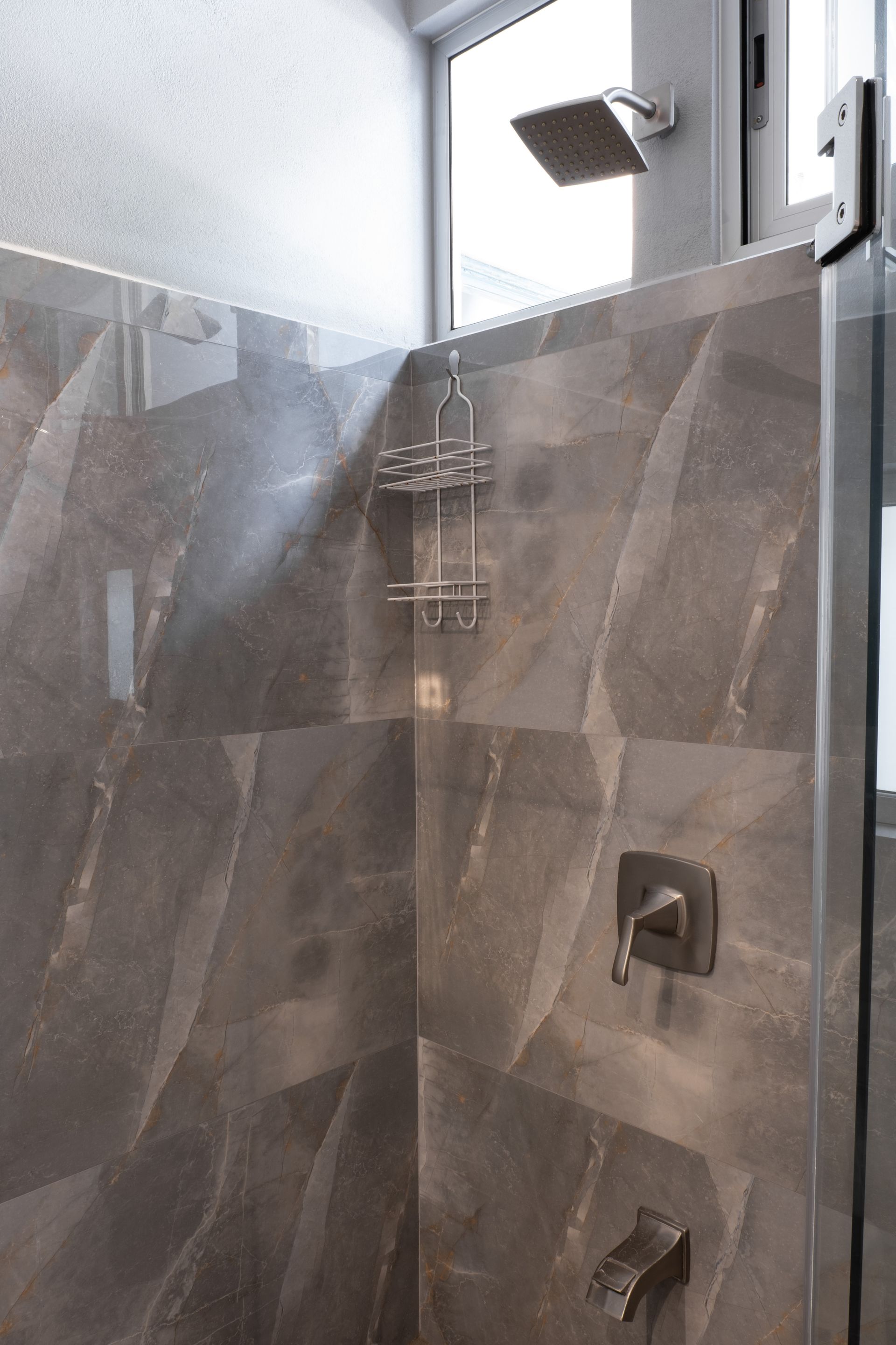 Modern shower with dark brown stone-patterned tiles, a rectangular shower head, a chrome caddy, and brushed metal fixtures.