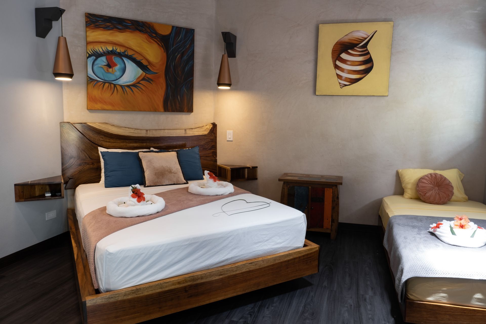 A hotel room with a queen bed featuring a live-edge headboard, a single bed, wall art, and ambient bedside lighting.
