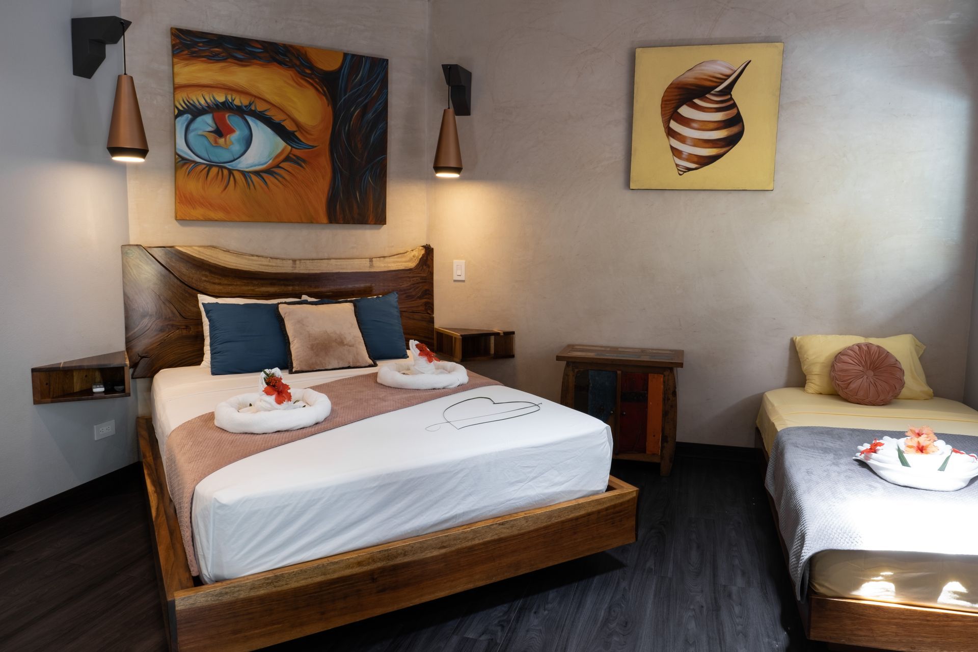A bedroom with a queen bed featuring a live-edge headboard, an adjacent twin bed, and two paintings on the gray walls.
