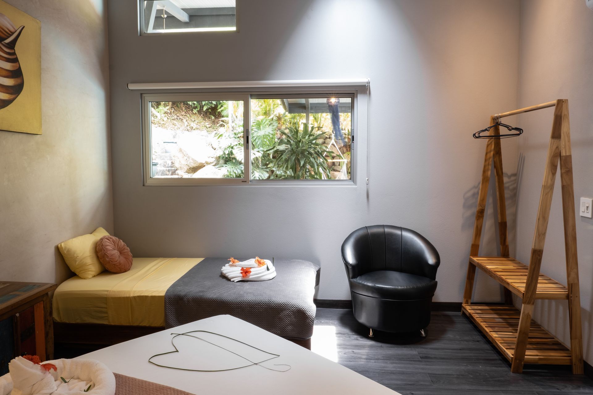 A modern bedroom featuring a bed with yellow and gray bedding, a black armchair, and a wooden garment rack against a wall.
