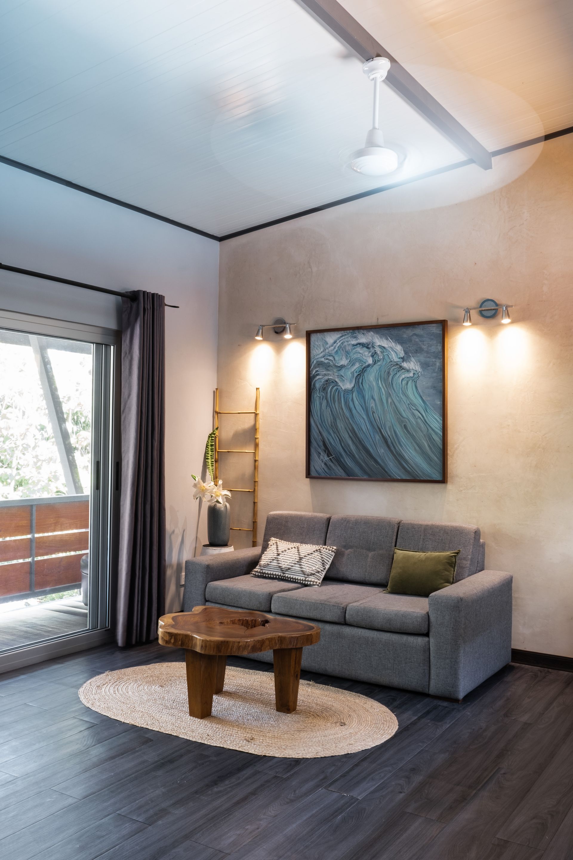 A modern living room with a grey sofa, a wooden coffee table, a textured rug, and a large ocean-themed wall painting.