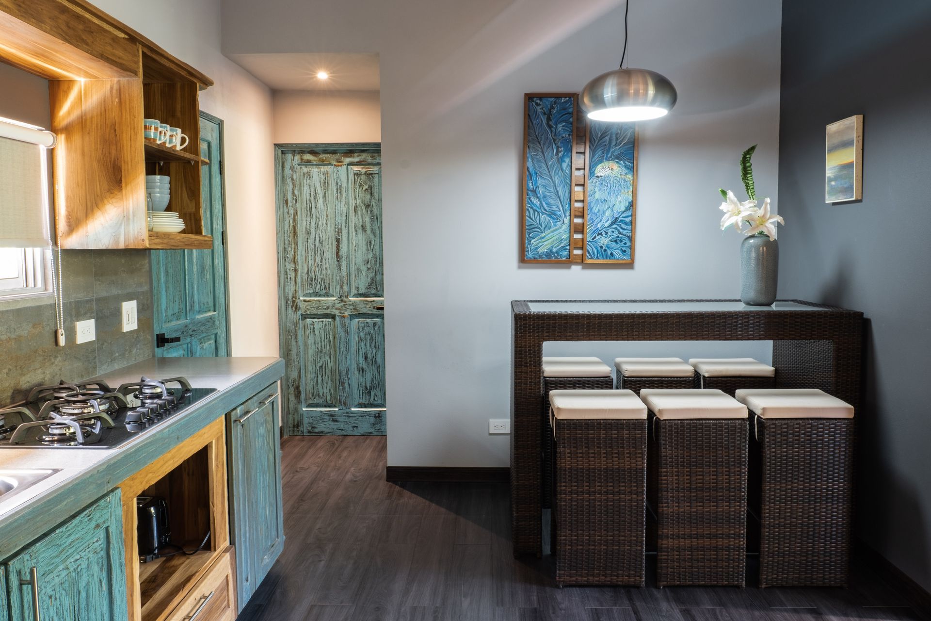 A kitchen featuring rustic, weathered teal cabinets, a dark wood table, and matching stools against a grey wall.