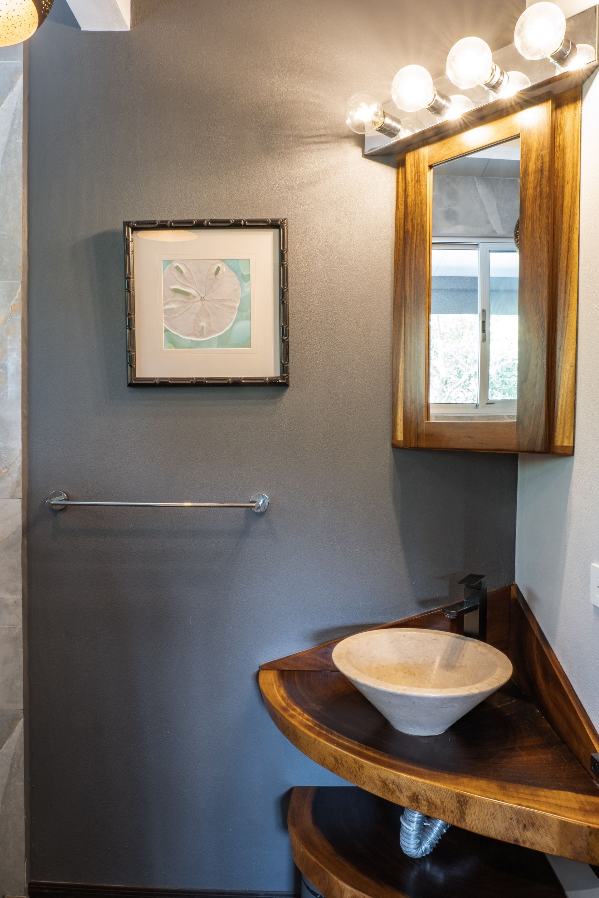 A corner vanity with a light stone vessel sink, wooden counter, and small medicine cabinet on a grey textured wall.
