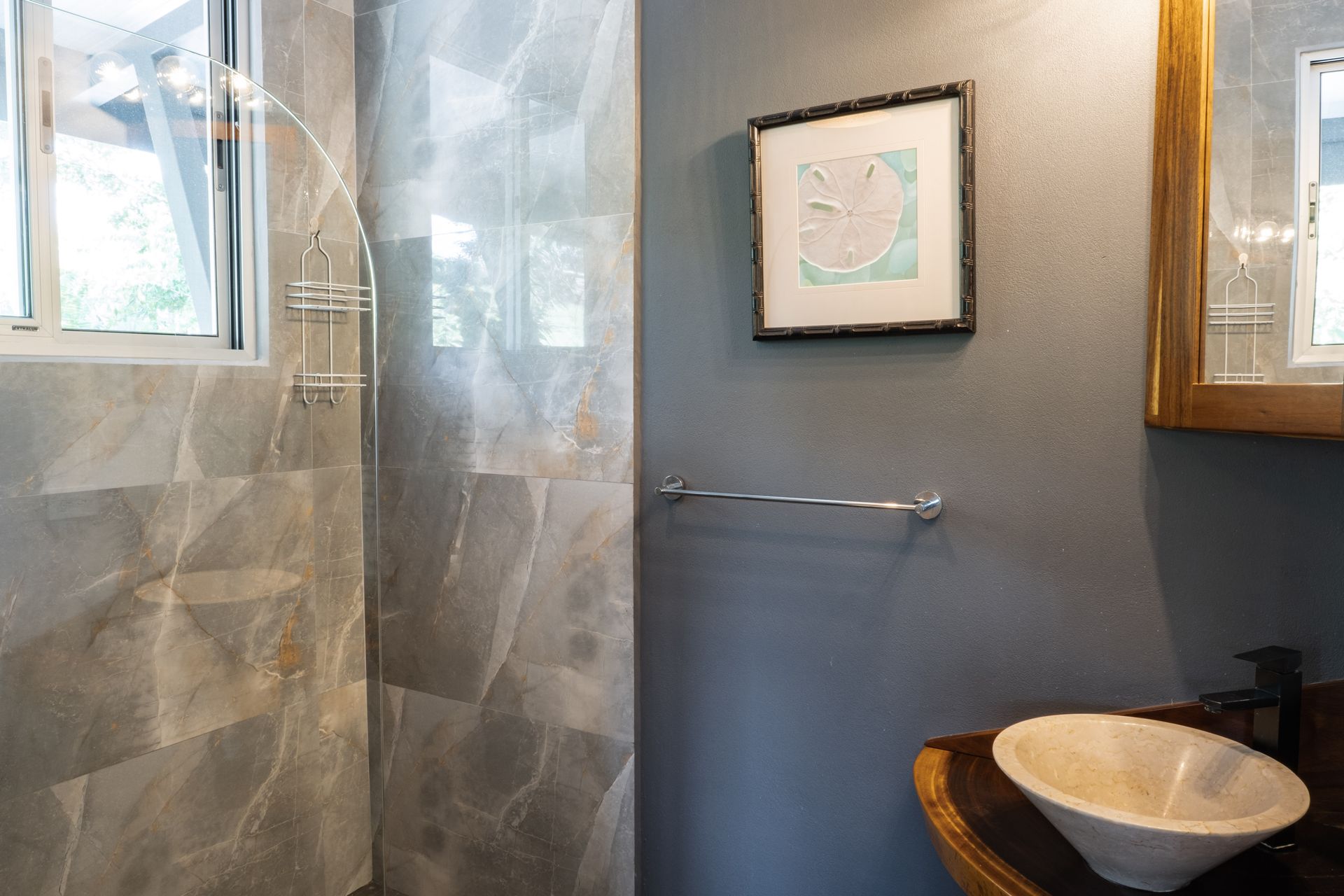 Modern bathroom with a marble-tiled shower, gray walls, a towel bar, and a rustic vessel sink on a wooden vanity.