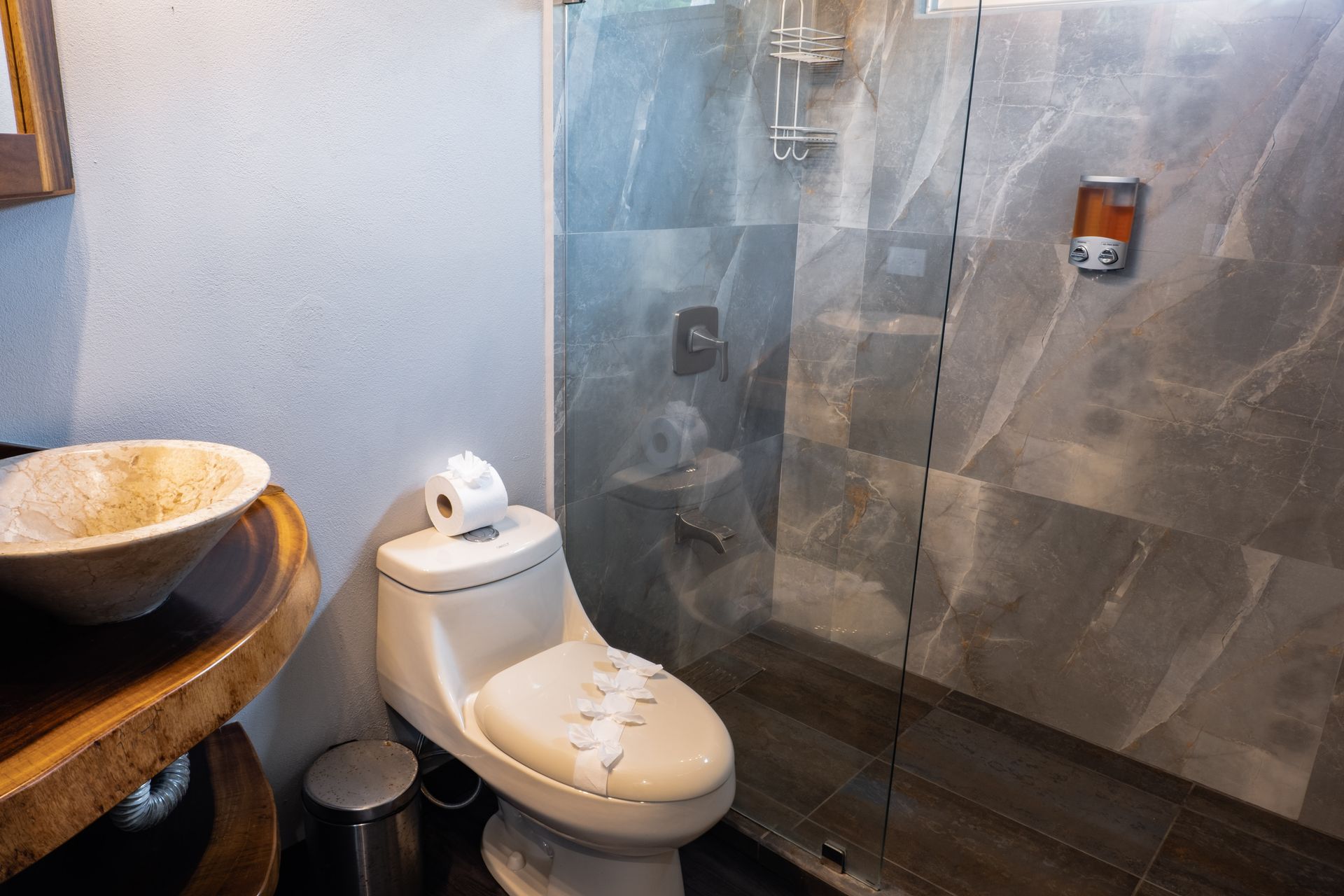 Modern bathroom with a white toilet, stone-tiled shower, and wooden sink counter