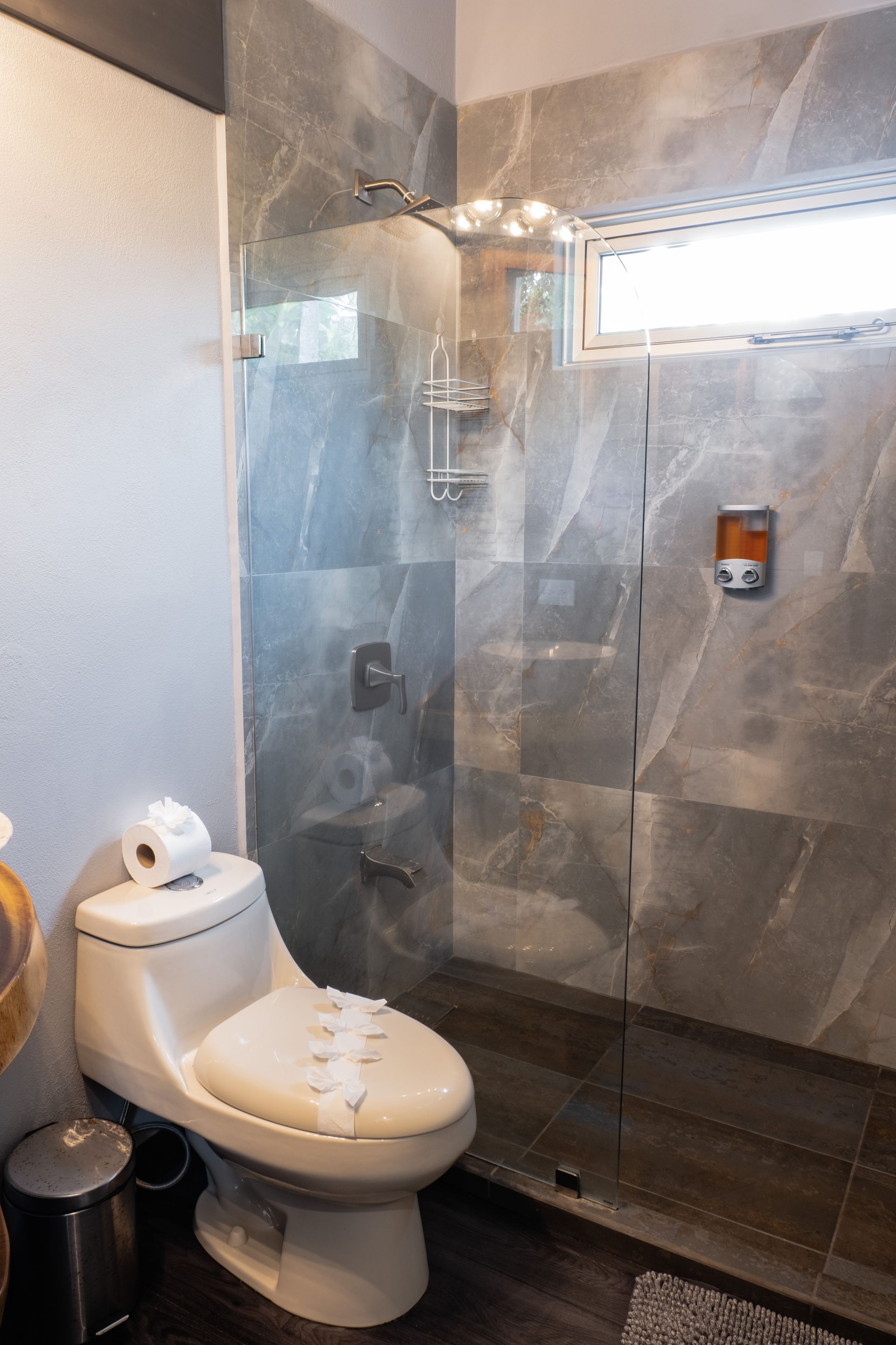 Small bathroom with a toilet, glass shower enclosure, and gray tiled walls.