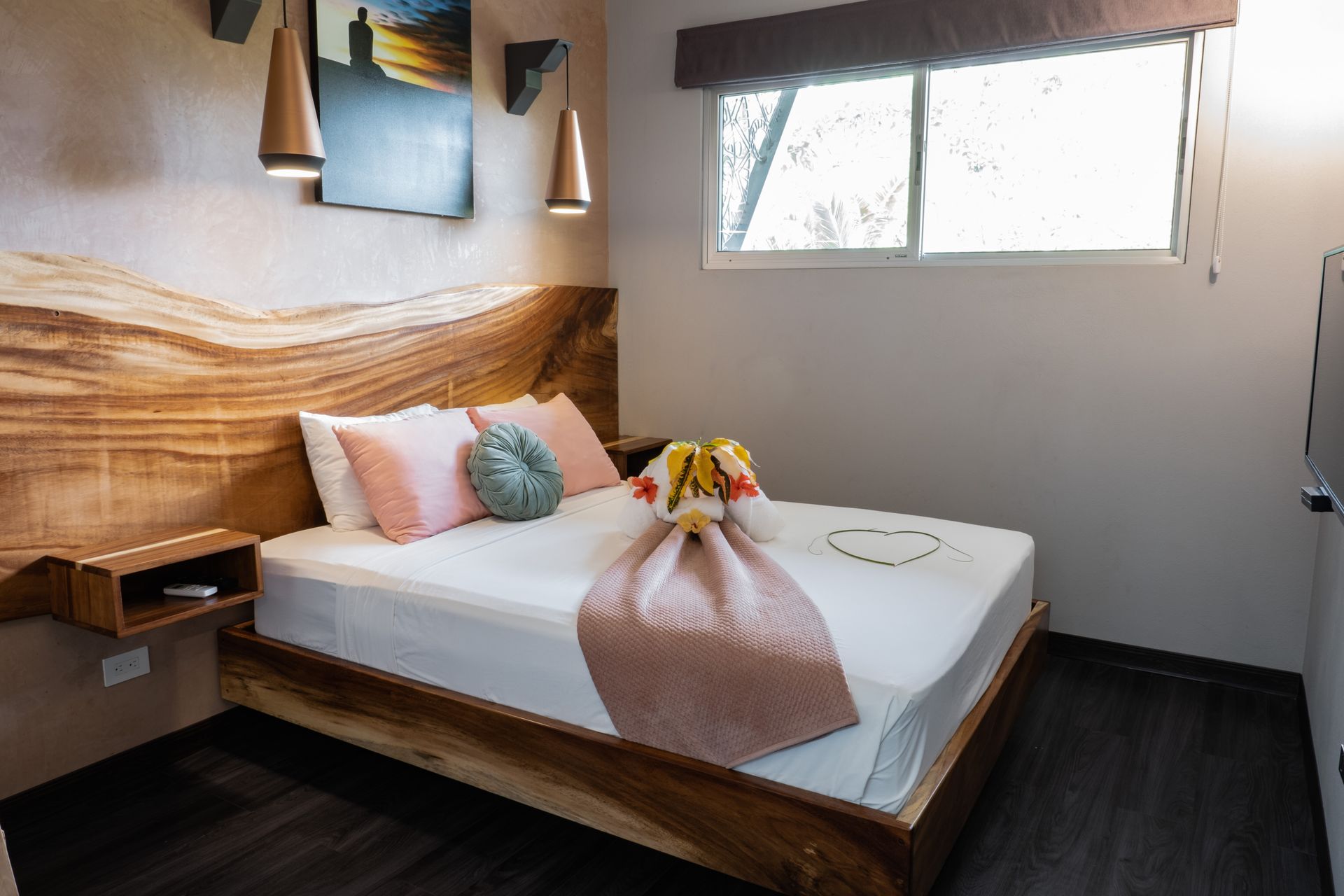 Modern bedroom with wooden bed, pink bedding, wall art, and a window letting in natural light