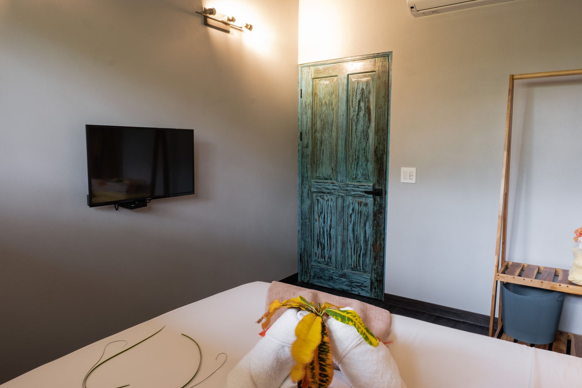 Hotel room with a bed, wall-mounted TV, blue door, and a window seat near the entrance