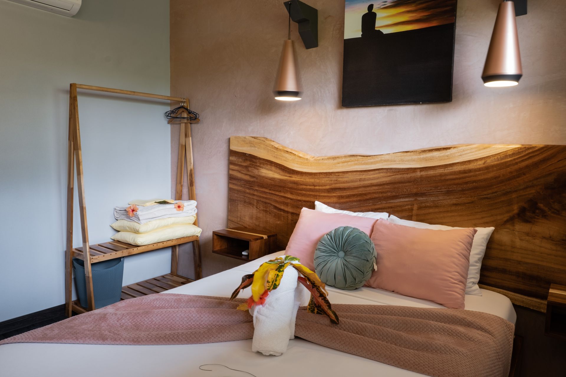 Cozy bedroom with a wood headboard, pink bedding, pendant lights, and a small side shelf.