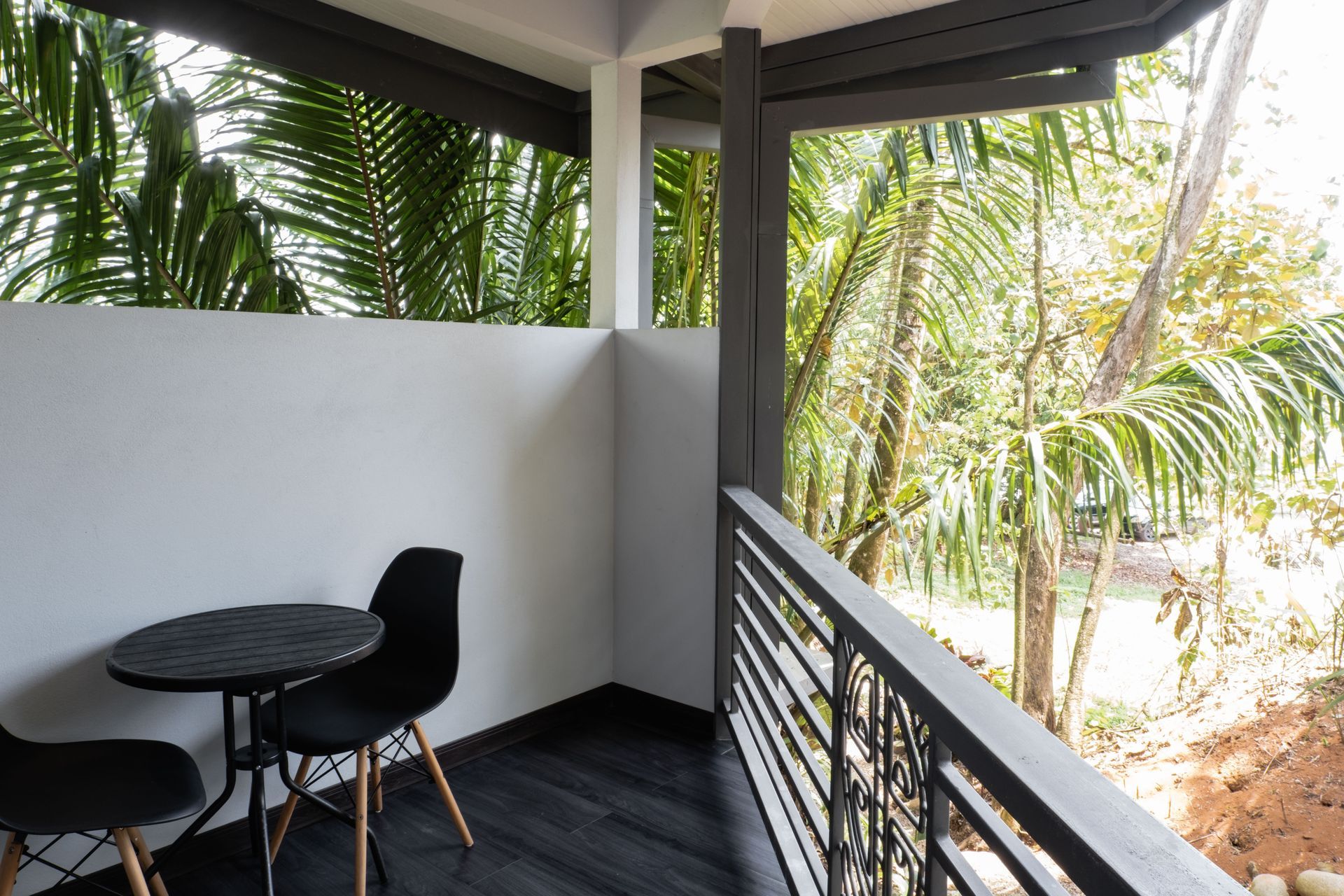 Balcony with black table and chairs, white walls, and palm trees beyond the railing