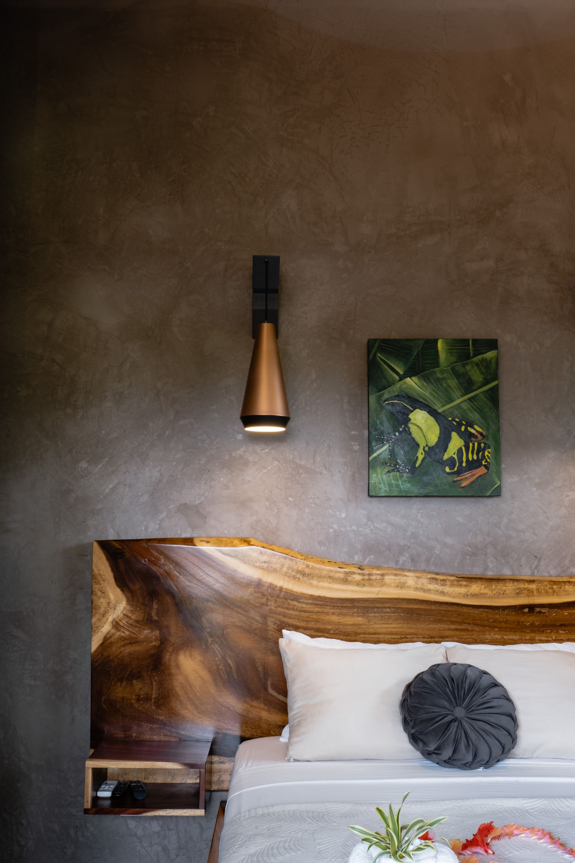 Modern bedroom with wood headboard, white bedding, wall lamp, and framed plant artwork.