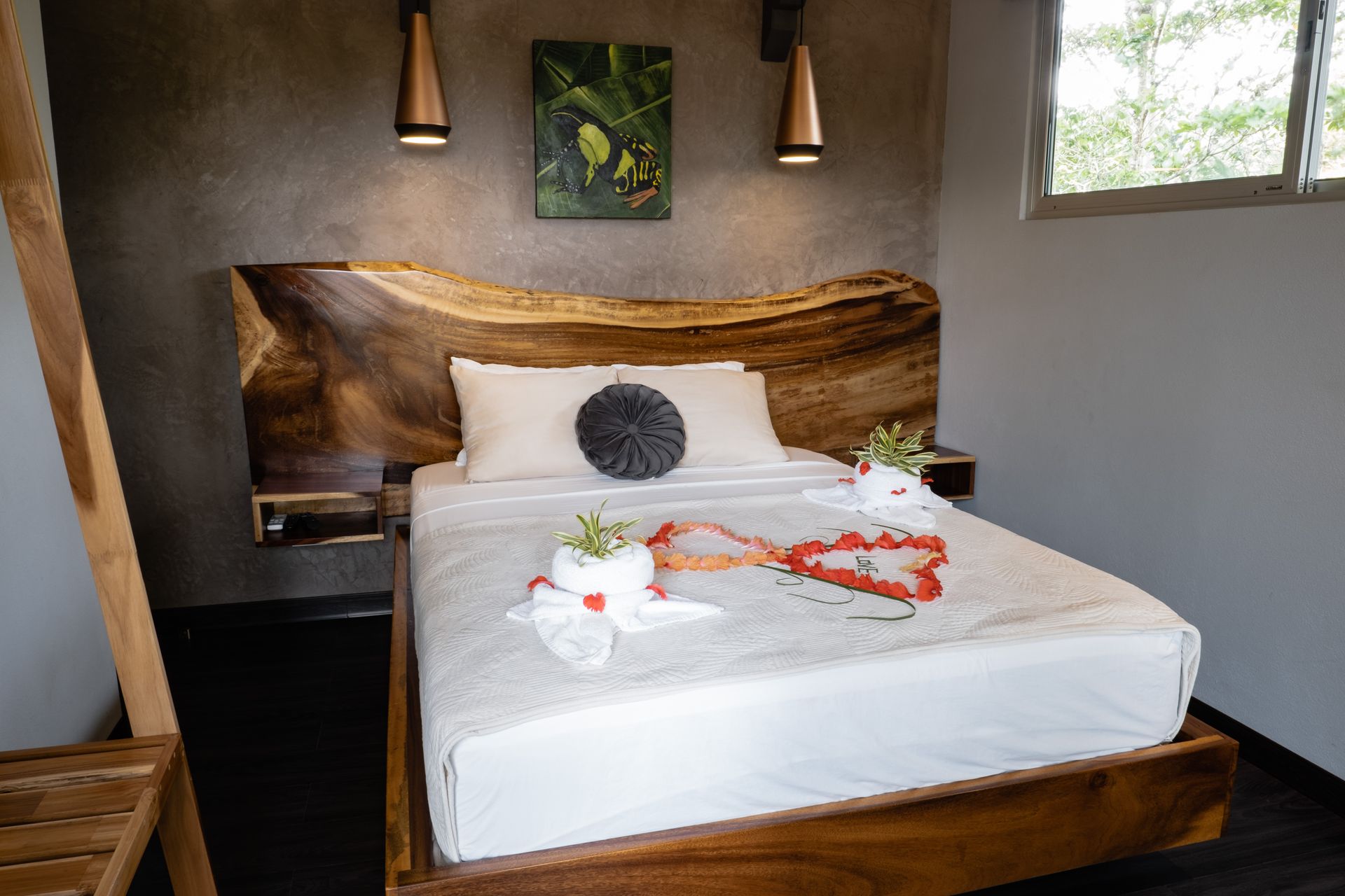Cozy bedroom with wooden bed, white linens, flower petals, and a window beside the bed