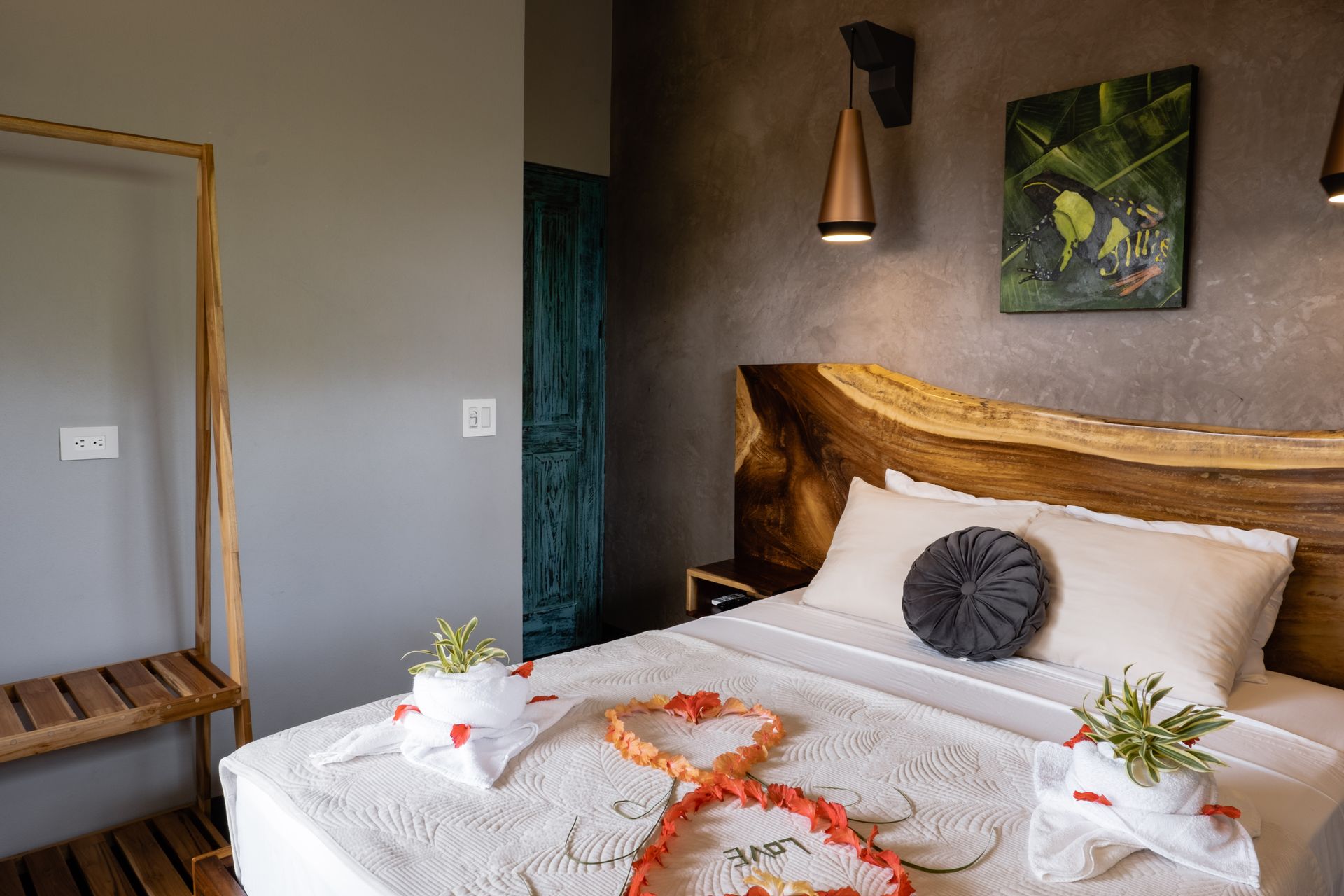 Cozy bedroom with a wooden bed, white linens, wall lamp, and bench beside a gray wall