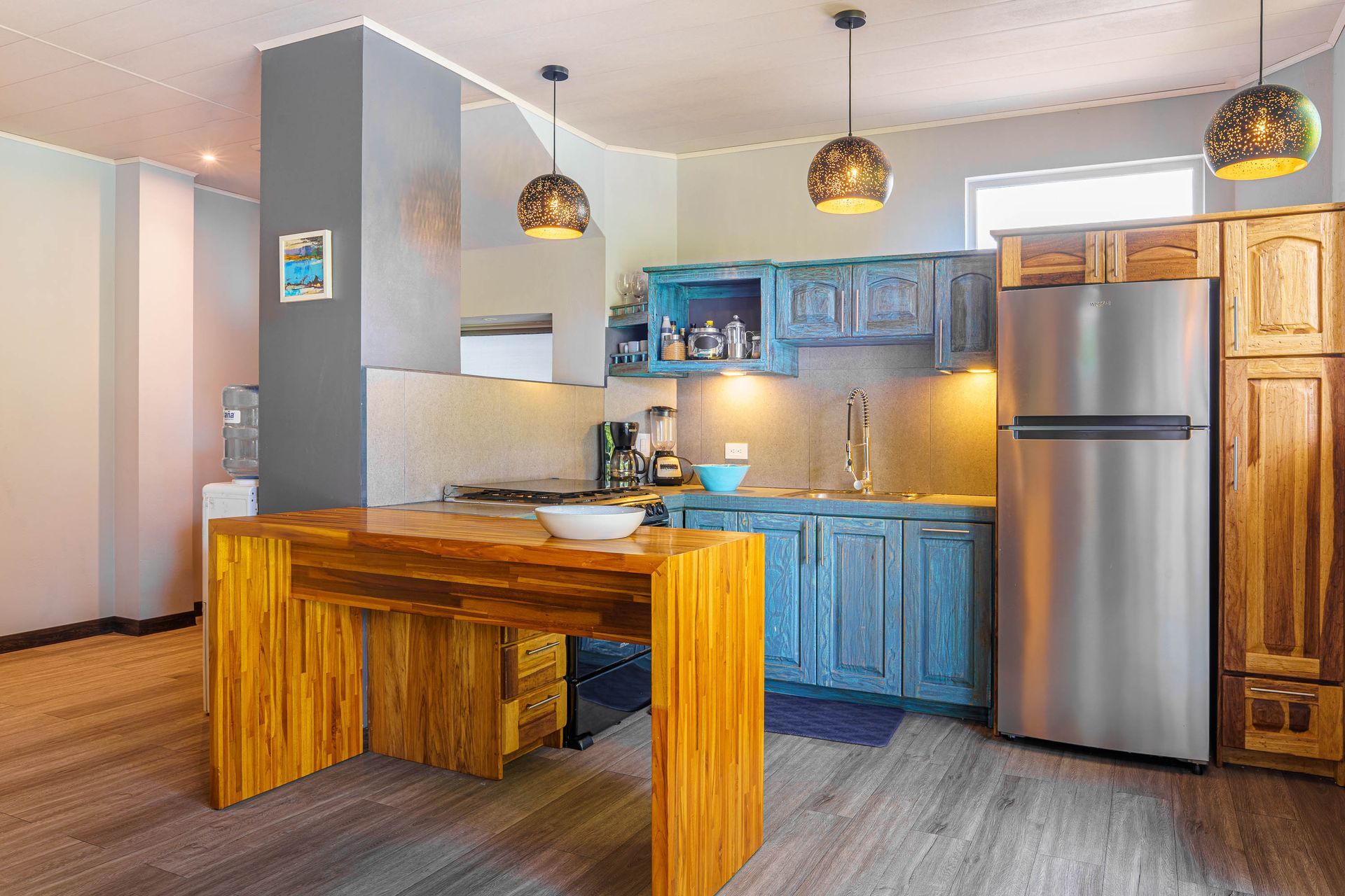 Modern kitchen with blue cabinets, stainless steel fridge, and wooden table under pendant lights
