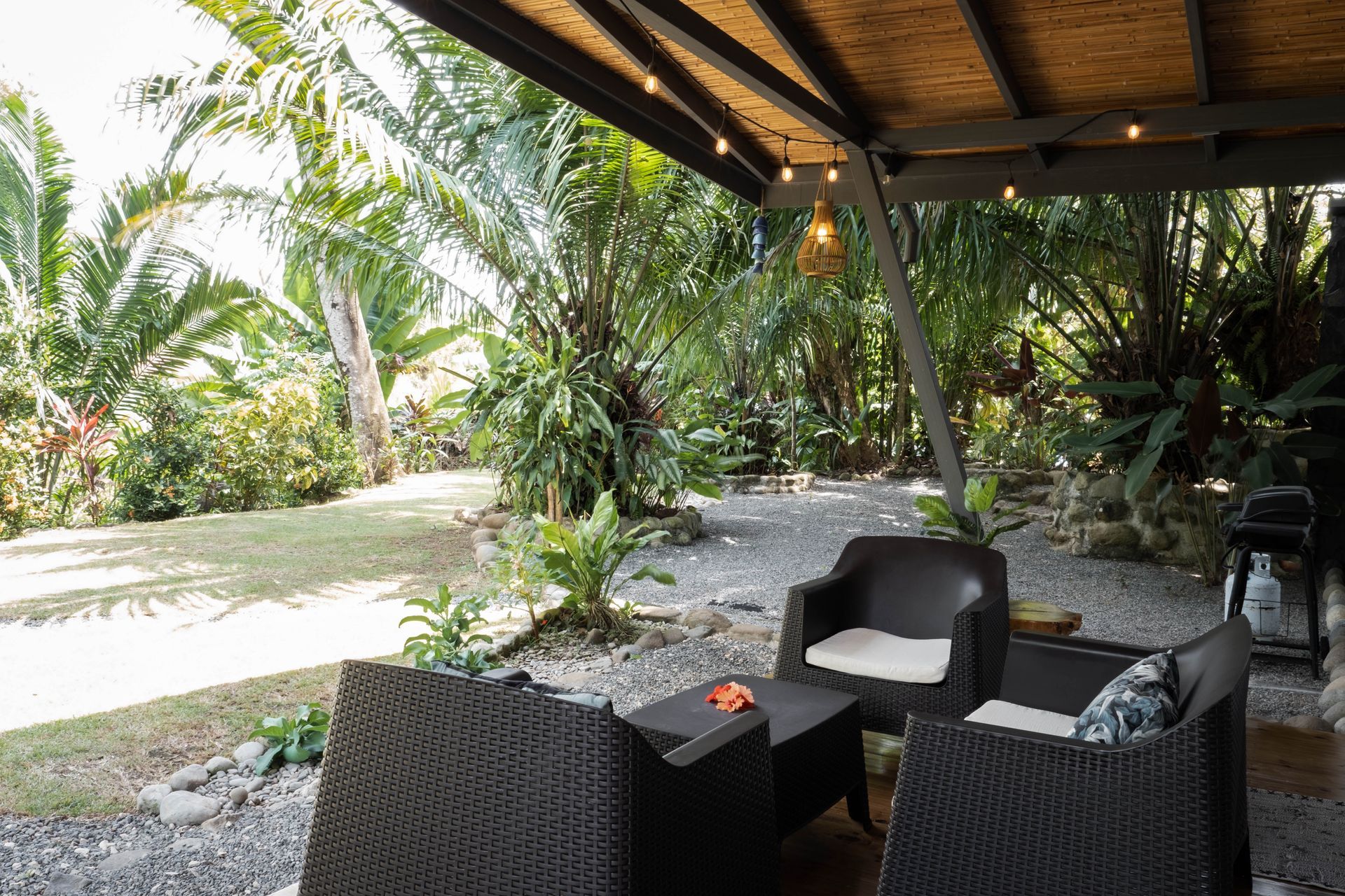 Covered patio seating overlooking a lush tropical garden and gravel path