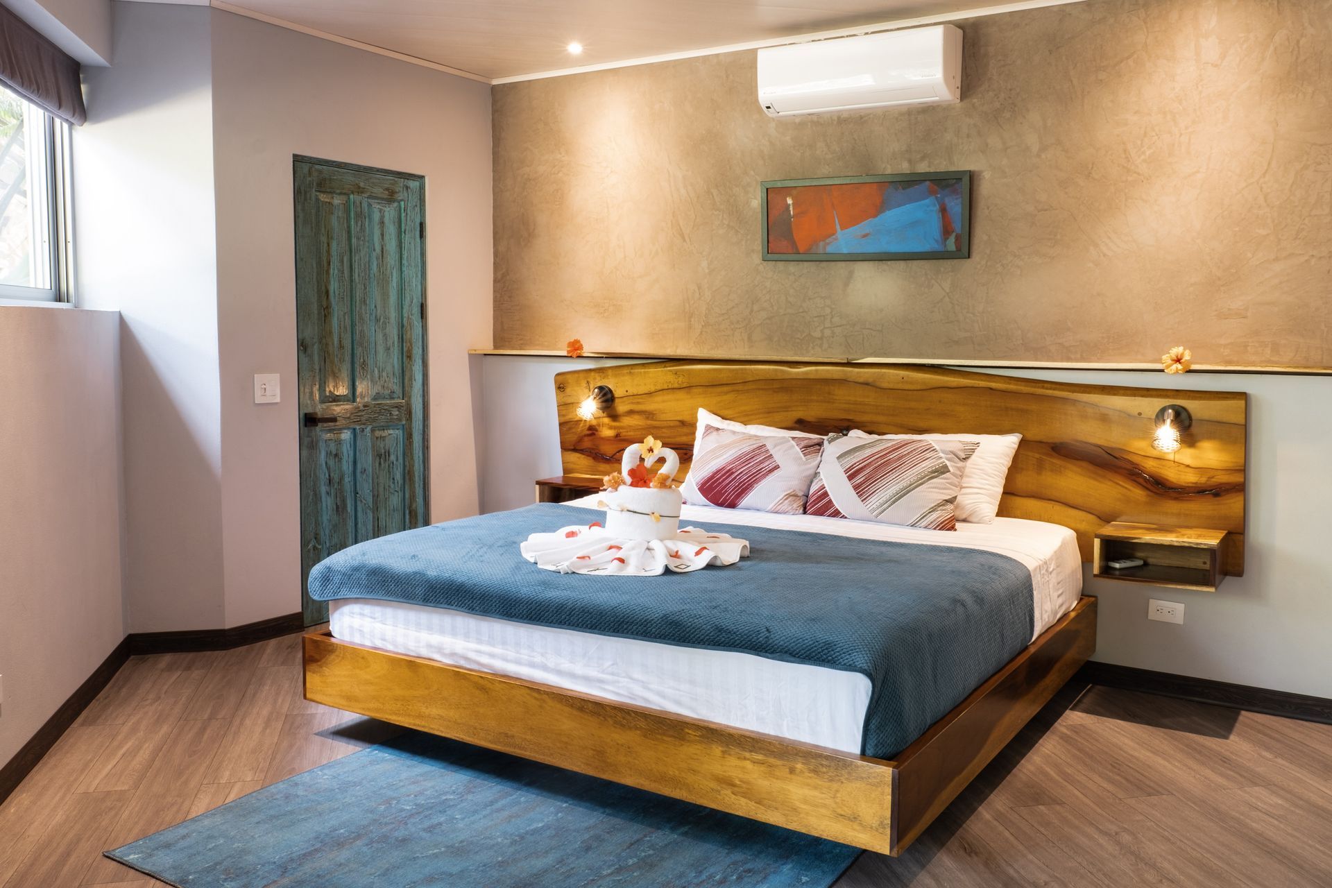 Modern bedroom with a wooden bed, blue bedding, blue rug, and warm tan walls