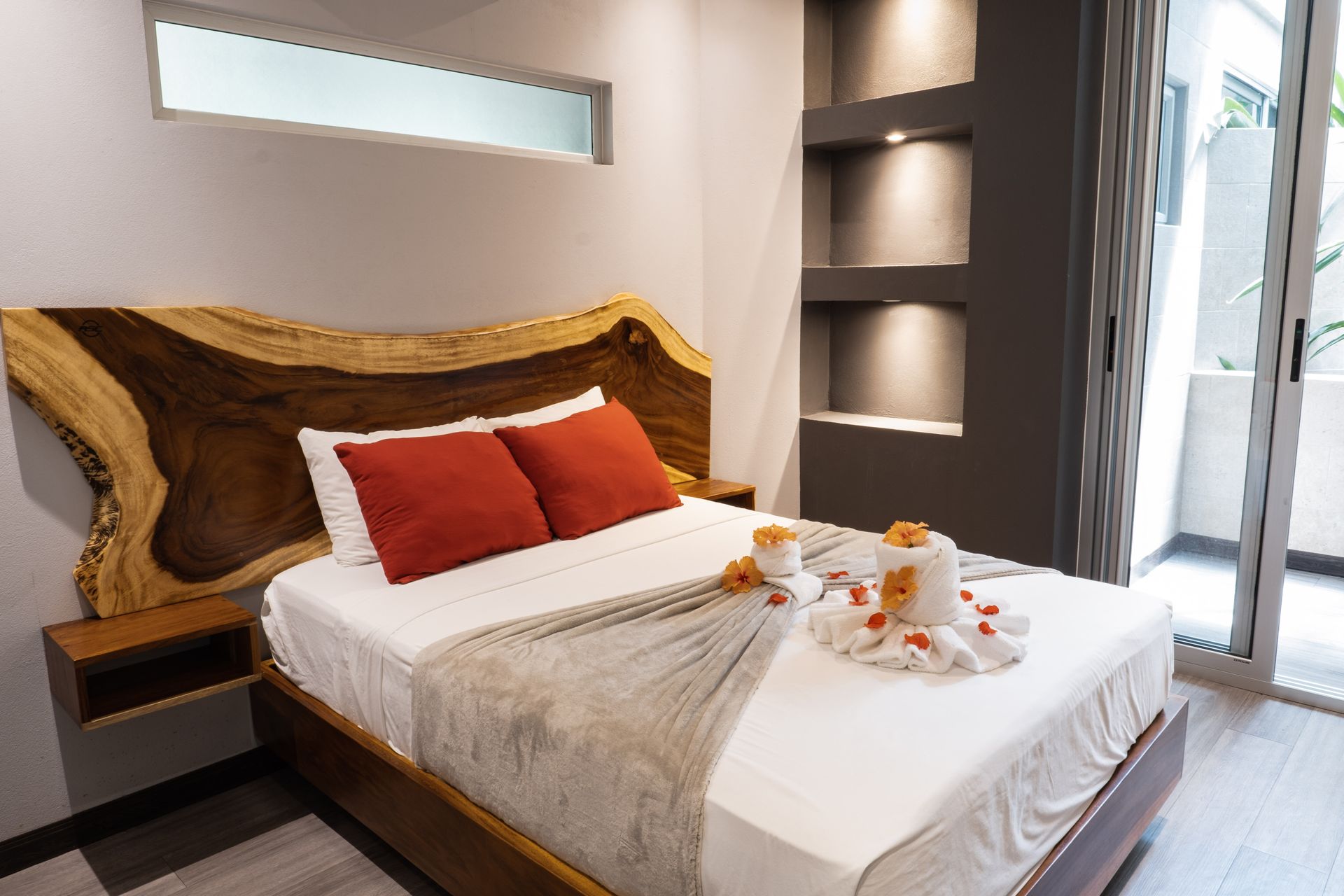 Modern bedroom with a wood headboard, red pillows, a made bed, and built-in wall shelves