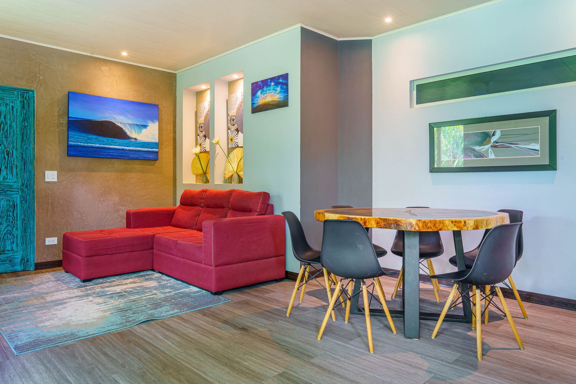 Modern living room with red sectional, round dining table, and teal accent wall on carpeted floor