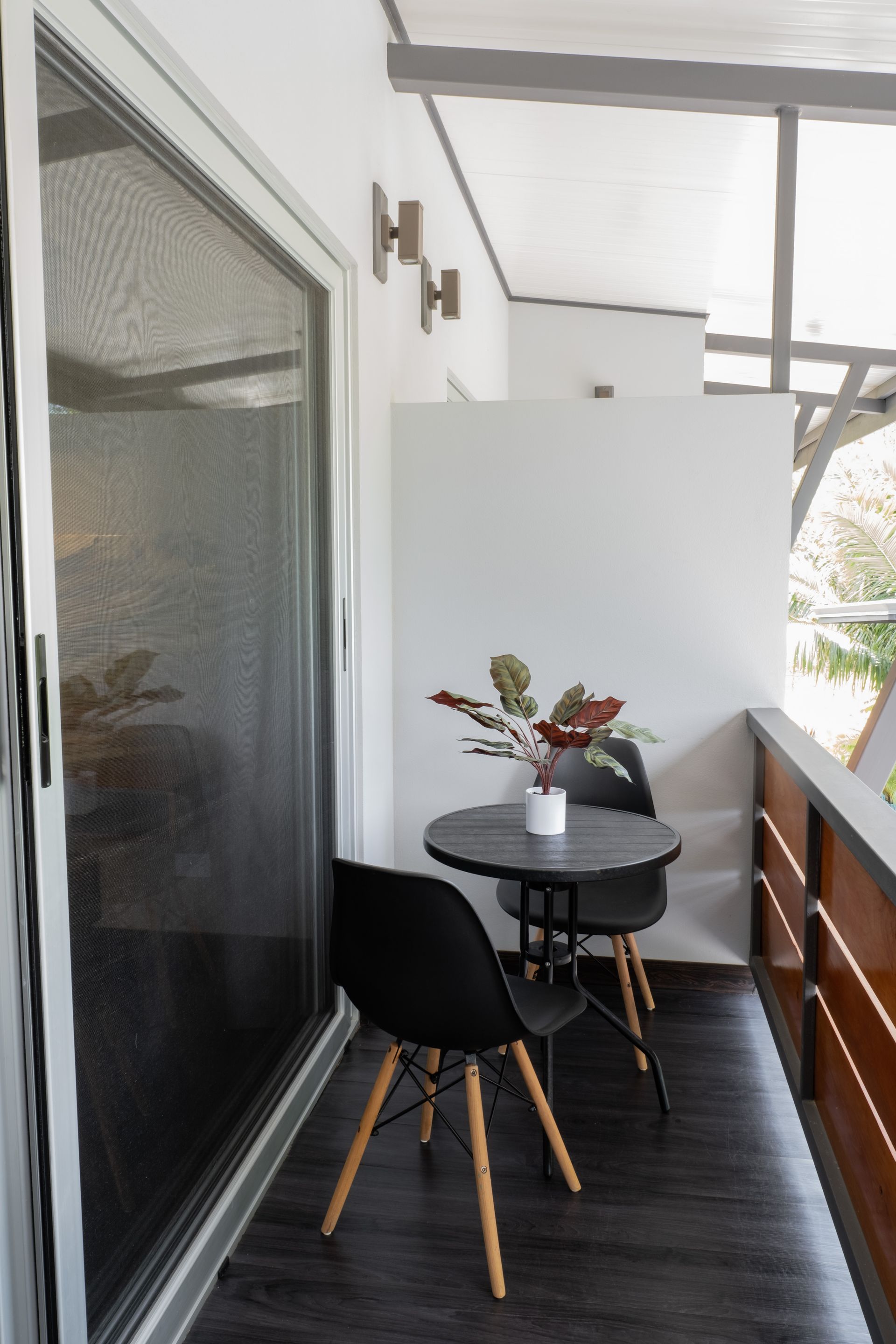 A balcony with two black chairs and a small round table holding a potted plant, set against a sliding glass door.